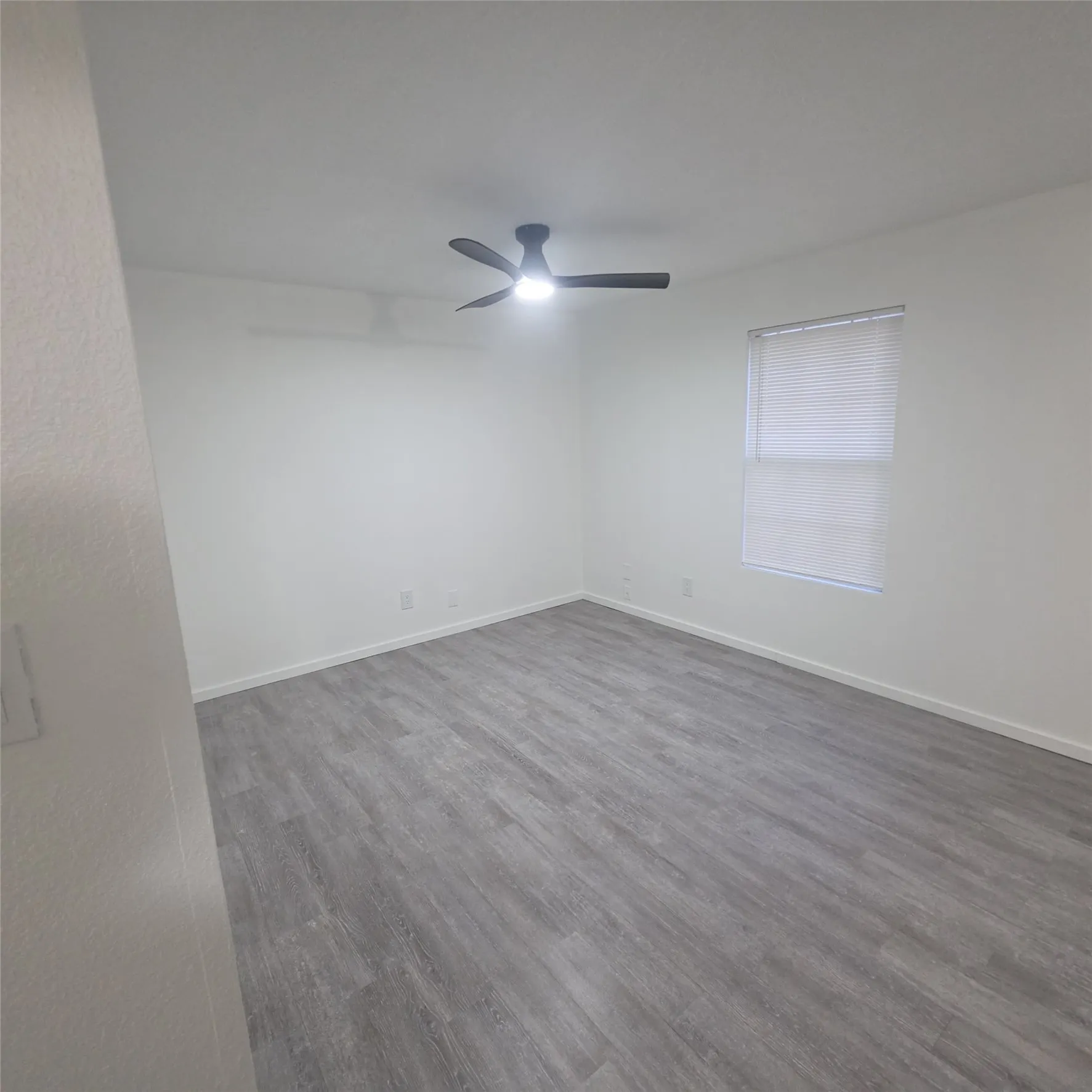 Spacious room featuring wood-finish flooring, a window with blinds, and a ceiling fan