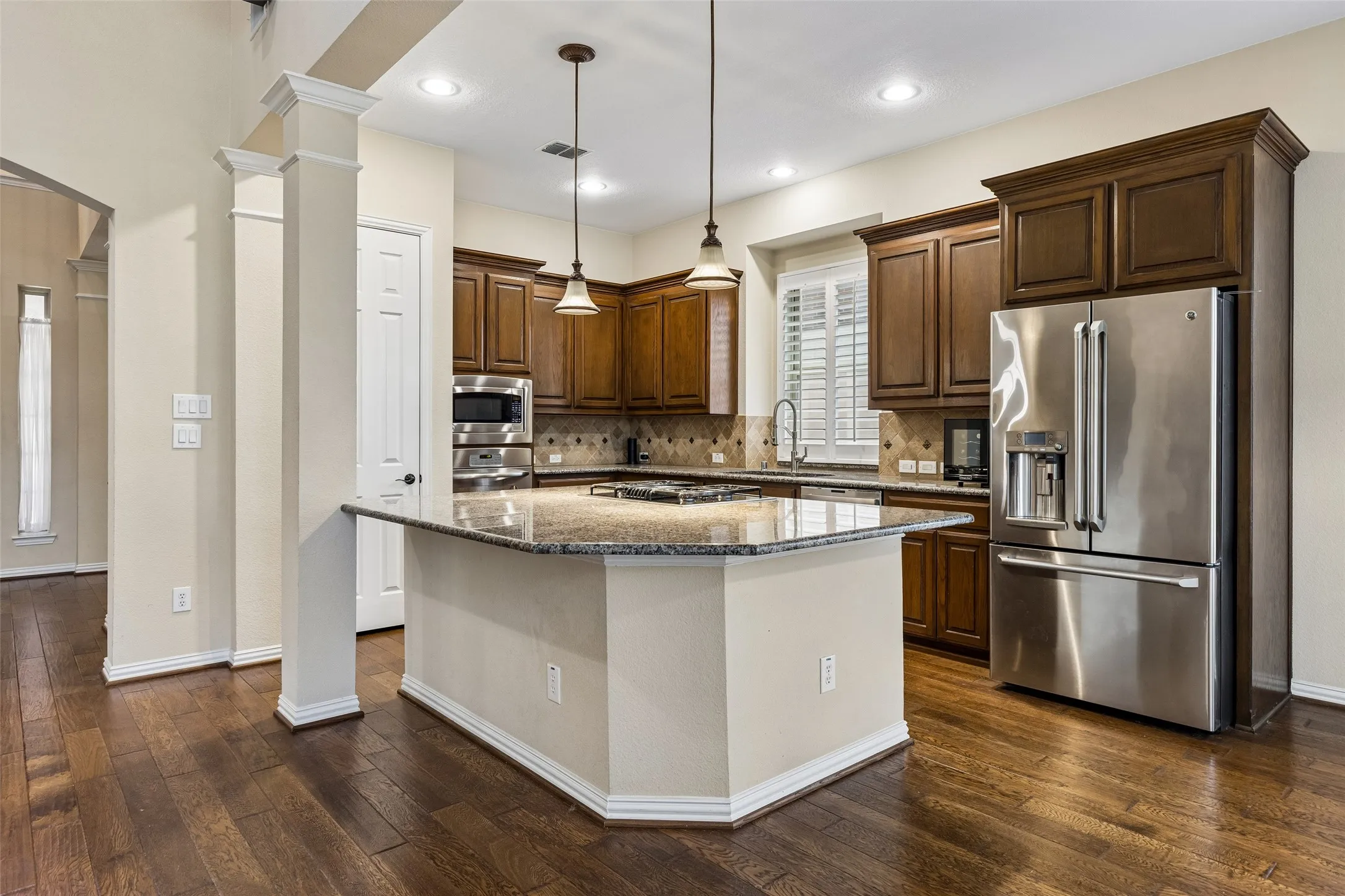 Kitchen featuring wood-finish flooring, a central island with granite countertop, dark wood cabinetry, and stainless steel appliances