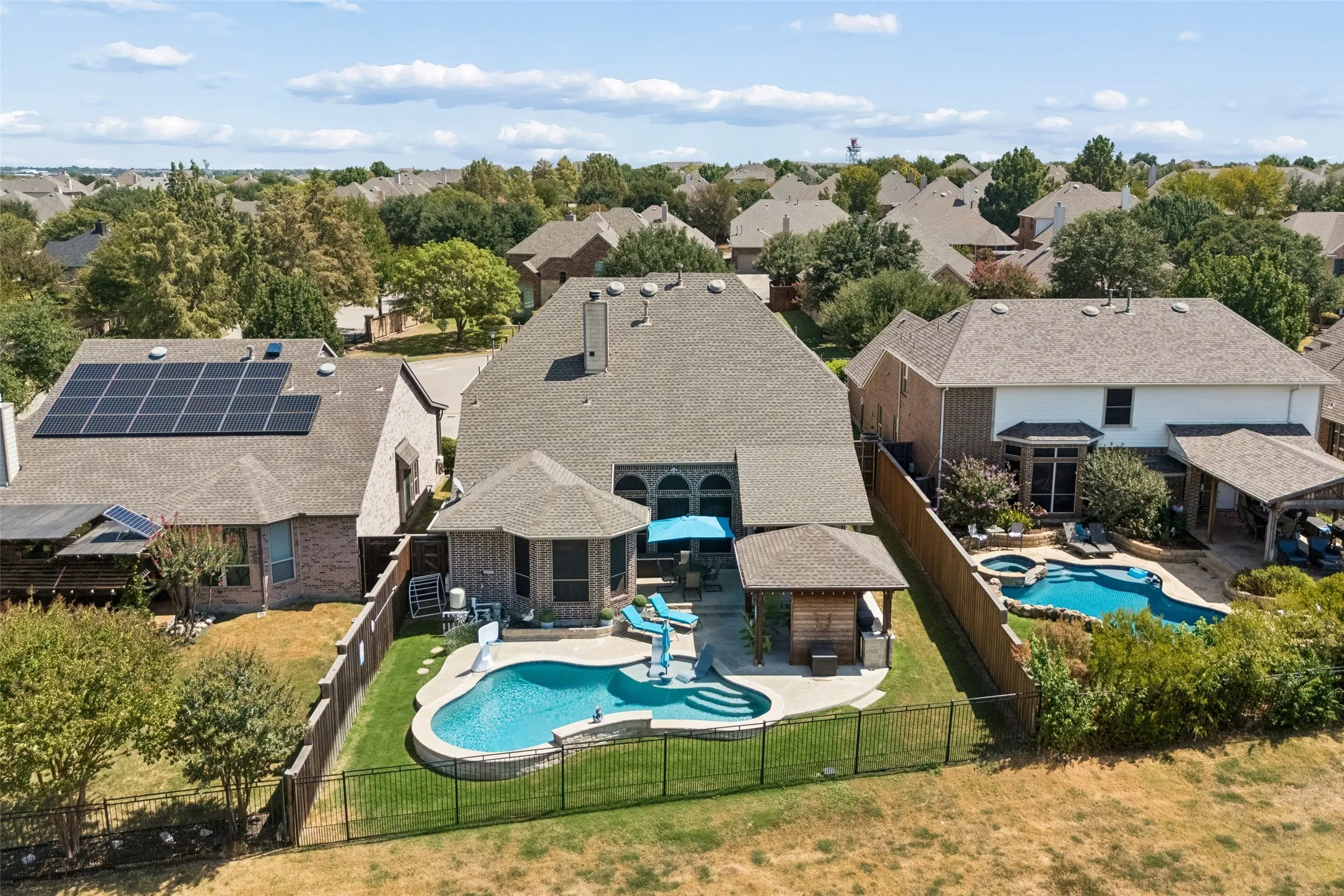 Resort-style backyard featuring a freeform pool, spa, built-in outdoor kitchen, and covered patio