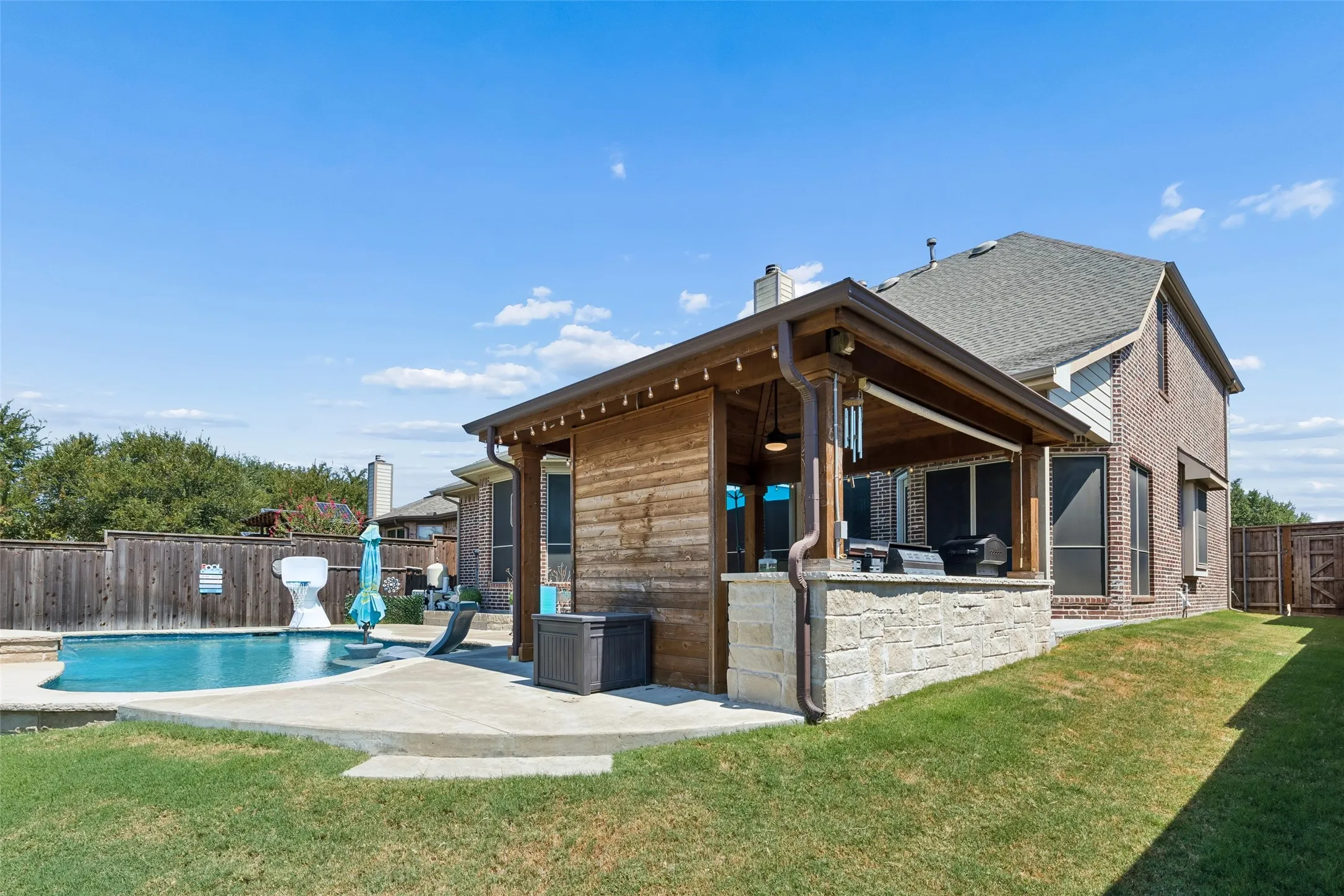 Outdoor living area featuring a covered patio with stone base, wood-paneled exterior, and recessed lighting