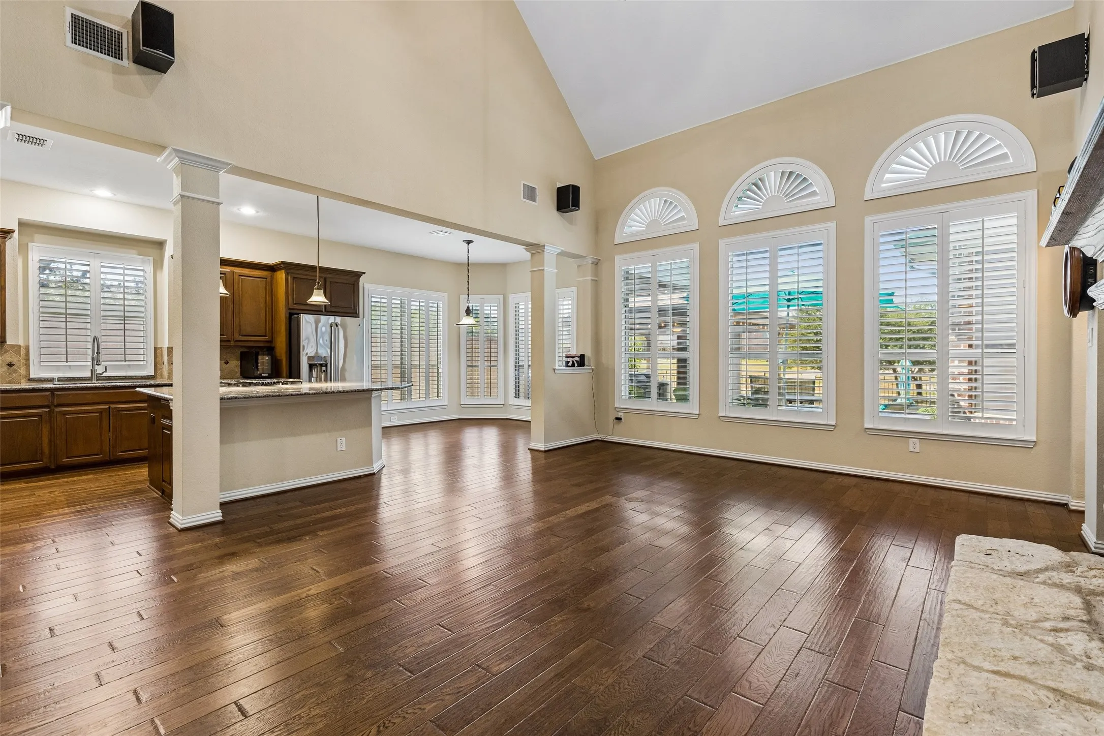 Vaulted ceiling with wood-finish flooring, stone-clad fireplace, and multiple windows with plantation shutters