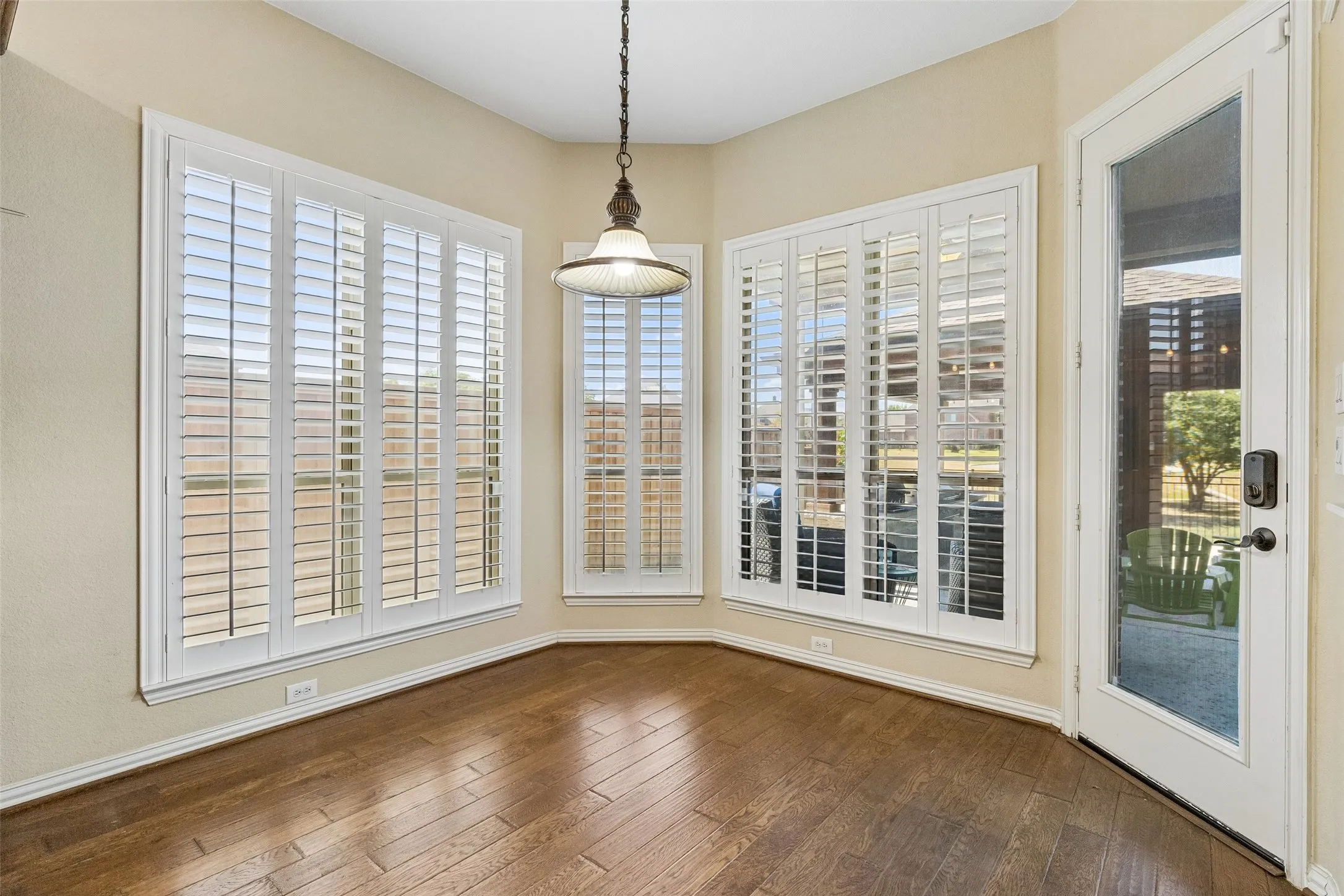 Wood-finish flooring, multiple windows with white plantation shutters, a glass-paneled door, and a decorative pendant light fixture