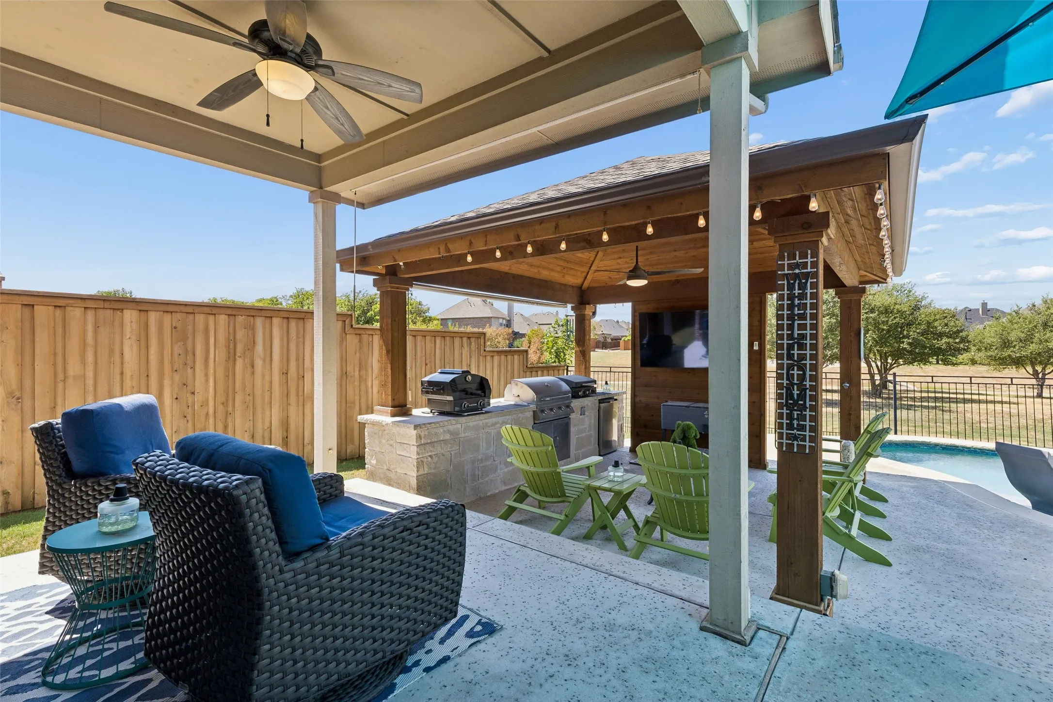 Covered patio with an outdoor kitchen, built-in television, and an adjacent swimming pool