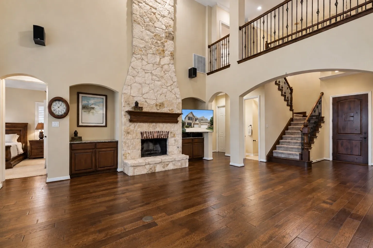Two-story living area featuring wood-finish flooring, a stone fireplace, and an open balcony overlooking the space