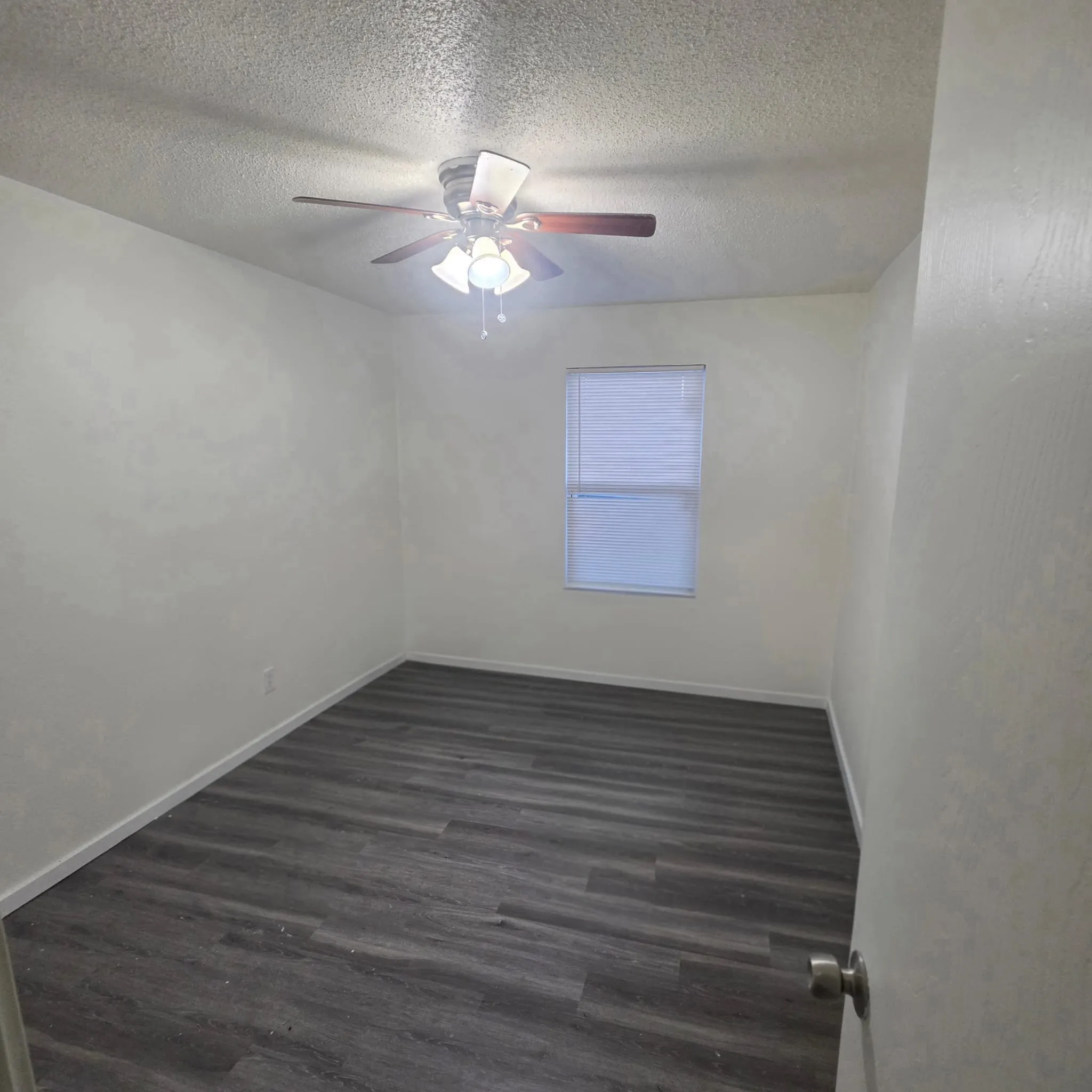 Neutral wall color, dark wood-finish flooring, ceiling fan with integrated lighting, window with blinds