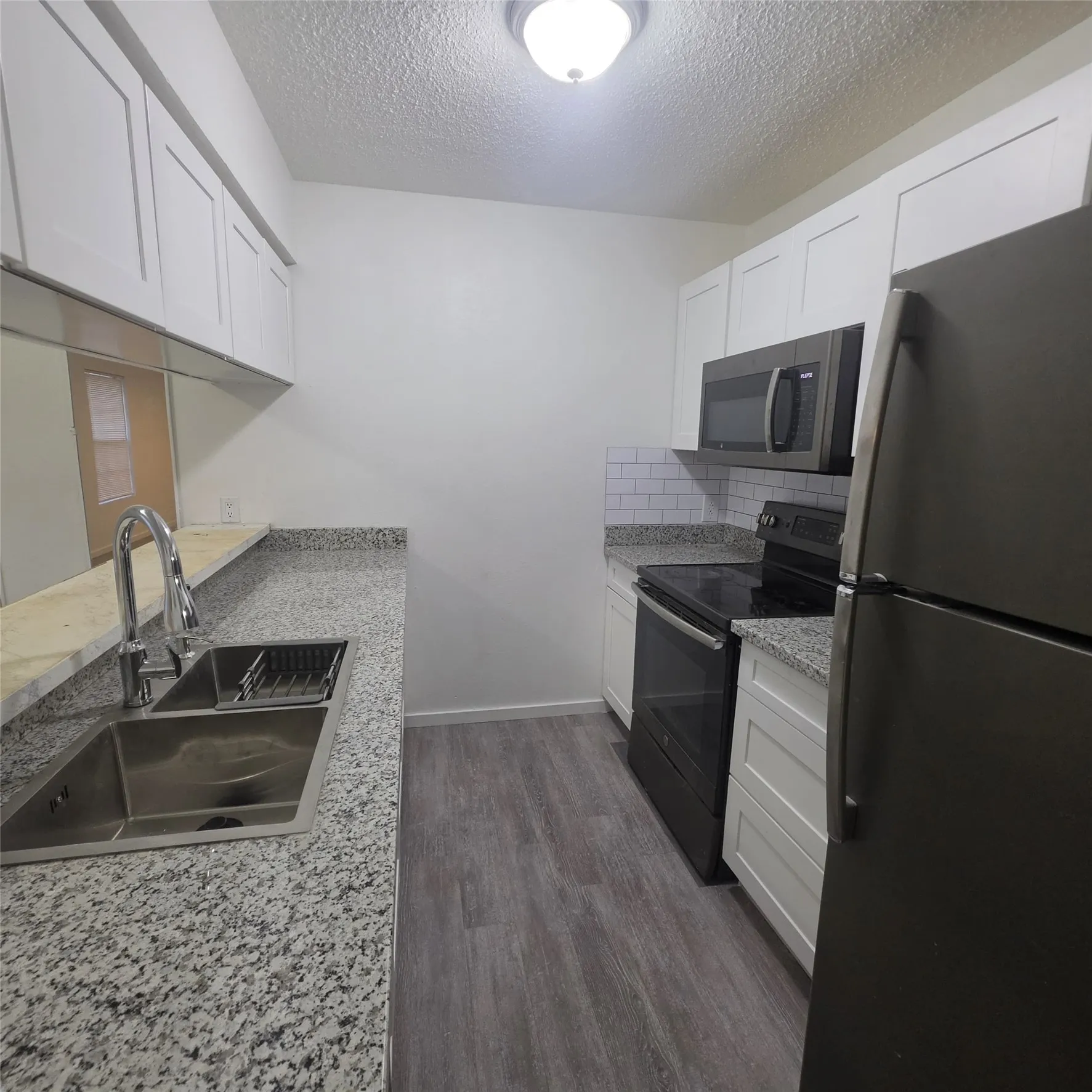 Kitchen featuring white shaker-style cabinetry, granite-finish countertops, subway tile backsplash, stainless steel sink, and wood-finish flooring