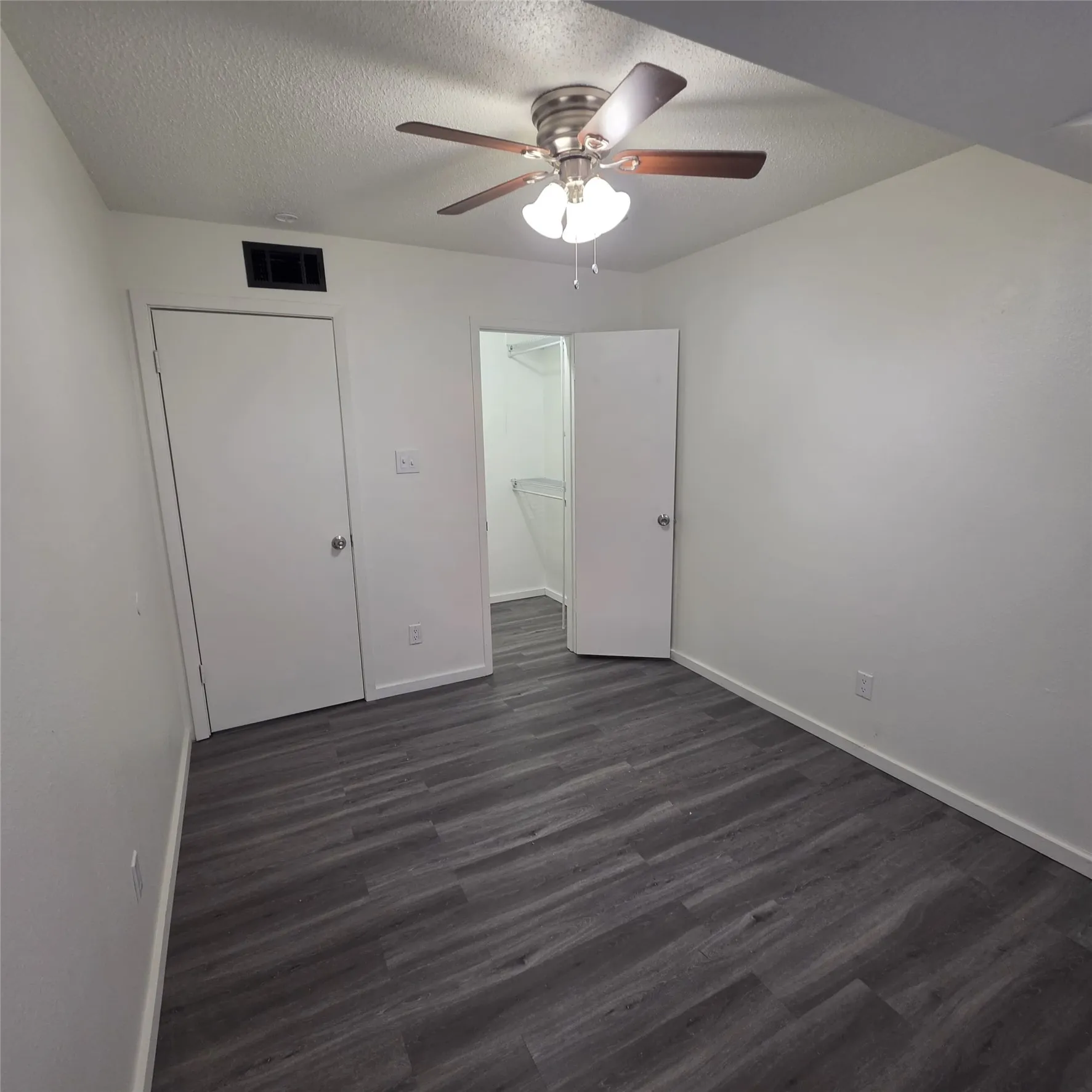 Wood-finish flooring, ceiling fan with integrated lighting, white walls, and a closet with shelving