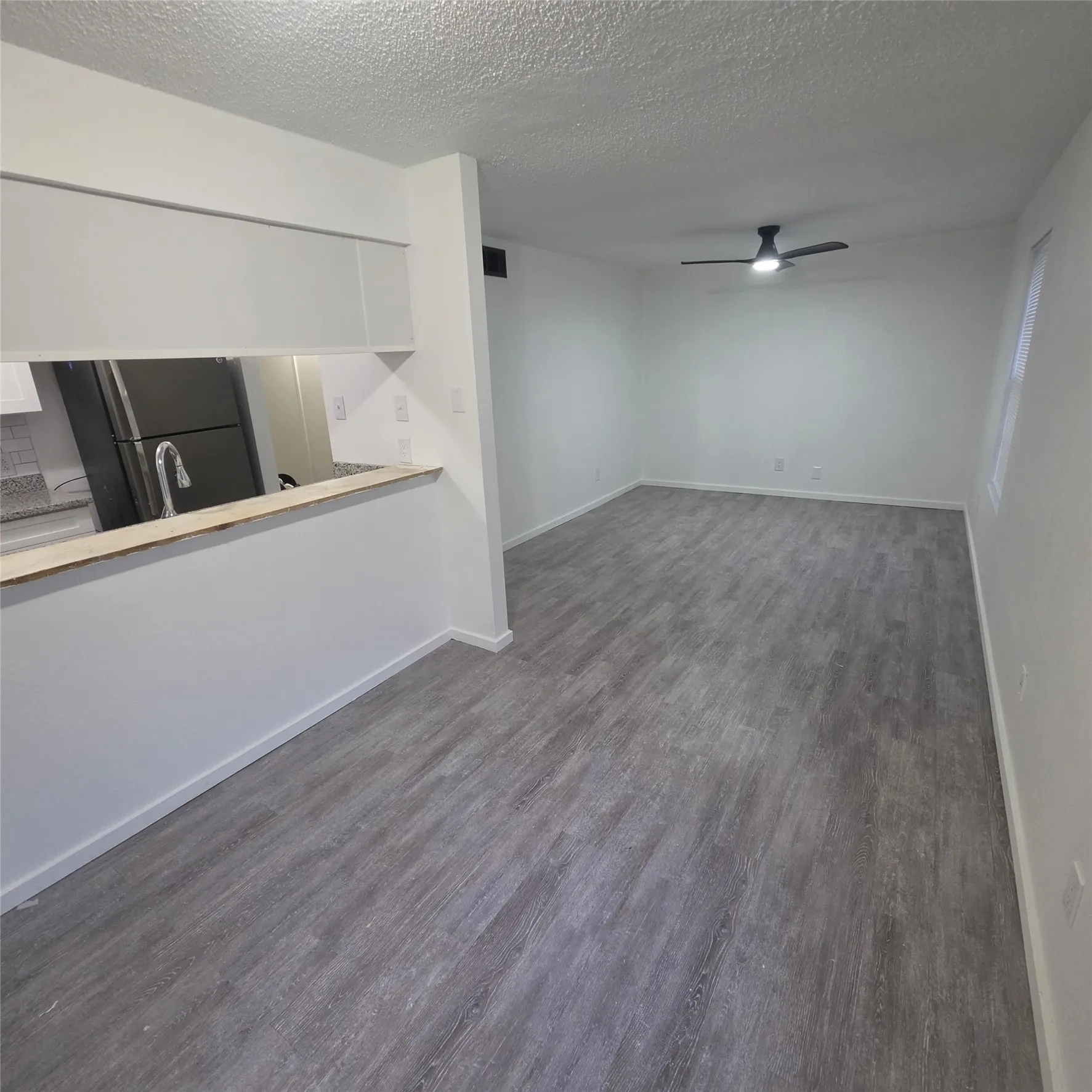 Spacious interior featuring wood-finish flooring, a contemporary ceiling fan, and a kitchen pass-through with granite countertops