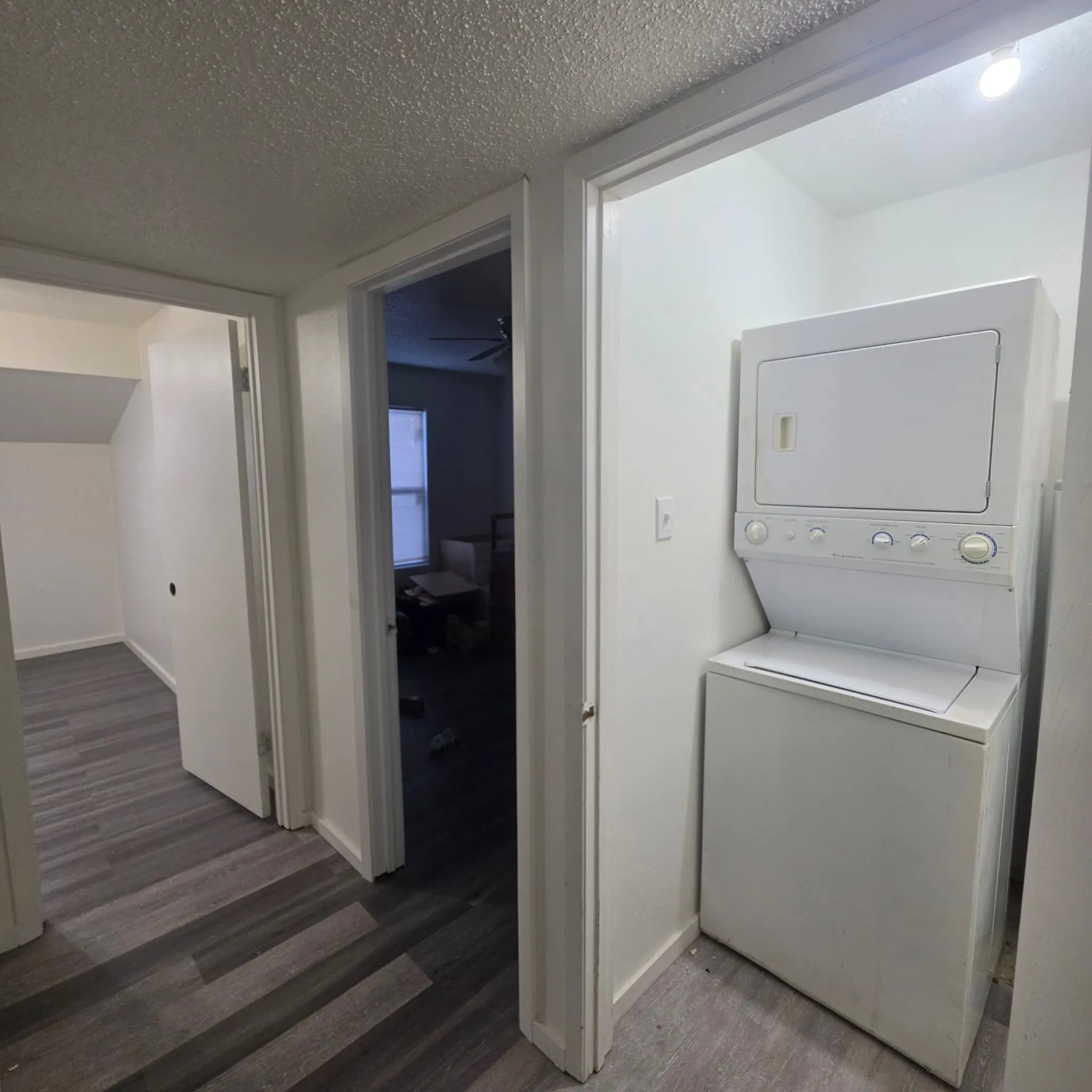 Laundry area with a stacked washer and dryer, wood-finish flooring, and light-toned walls