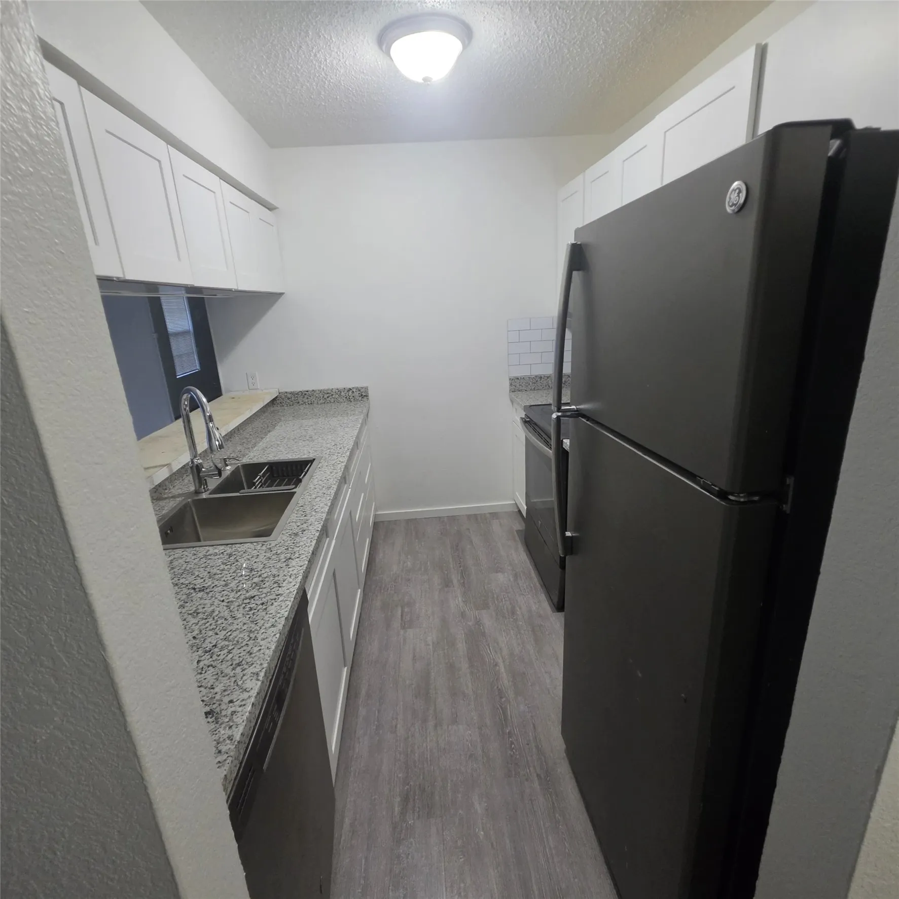 Galley kitchen featuring white cabinetry, light-toned countertops, a stainless steel double basin sink with a high-arch faucet, and wood-finish flooring