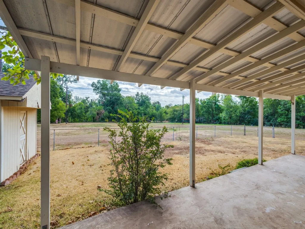 Large, covered patio area with concrete flooring and a corrugated metal roof. A chain-link fence encloses a smaller portion of yard creating a safe place for pets and children.