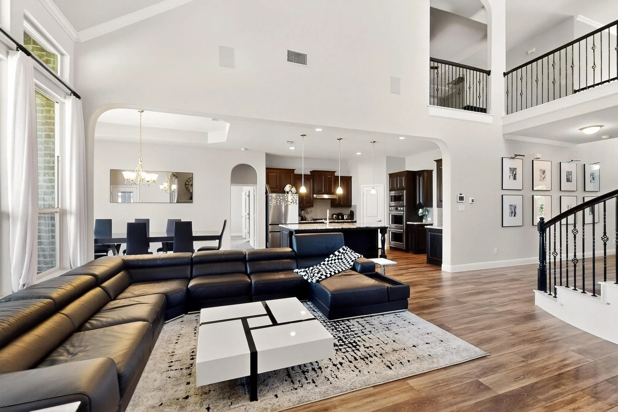 Living area with arched walkways, a chandelier, high vaulted ceiling, light wood-type flooring, and healthy amount of natural light
