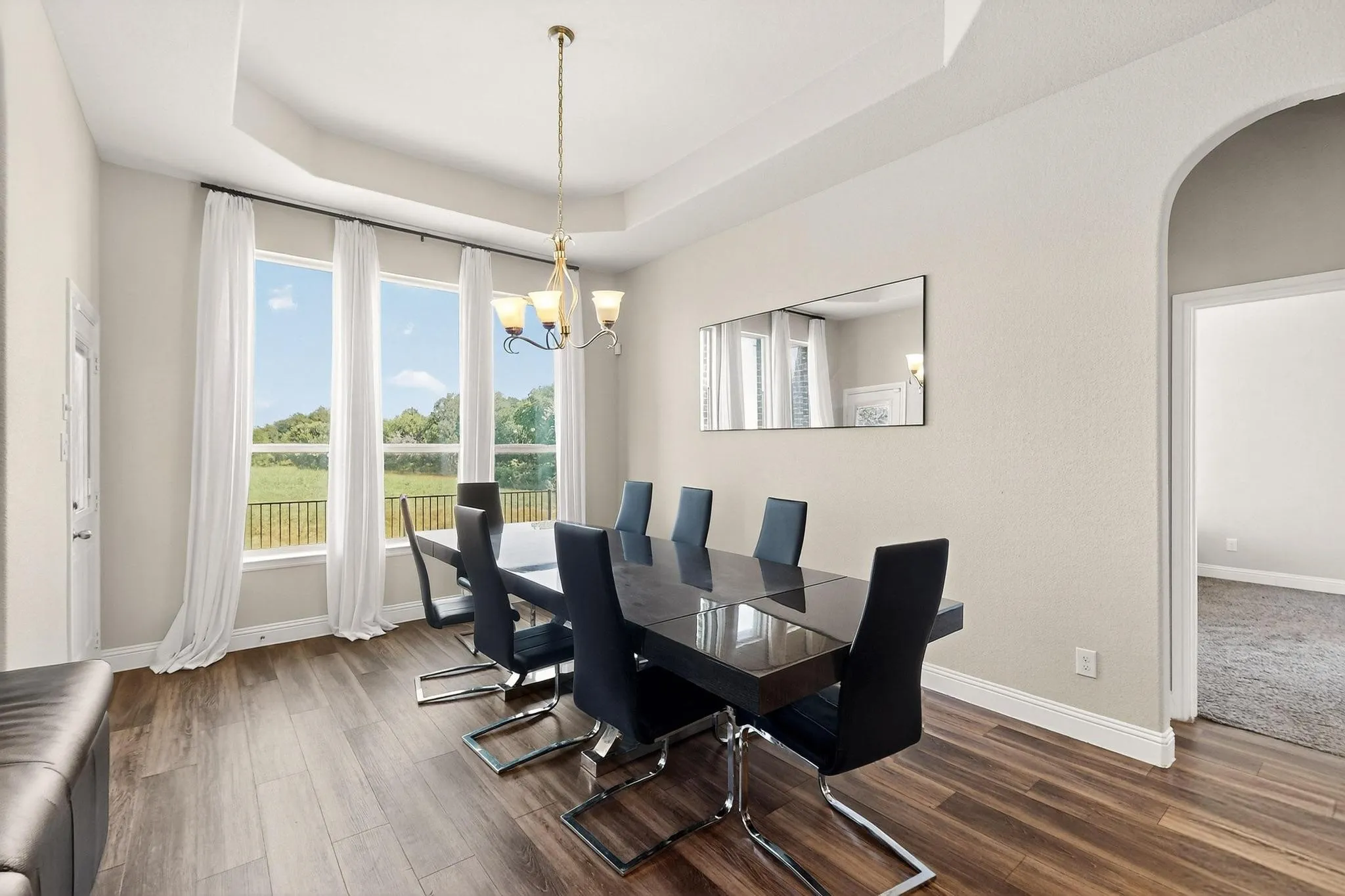 Dining room with a tray ceiling, dark wood finished floors, arched walkways, and a chandelier