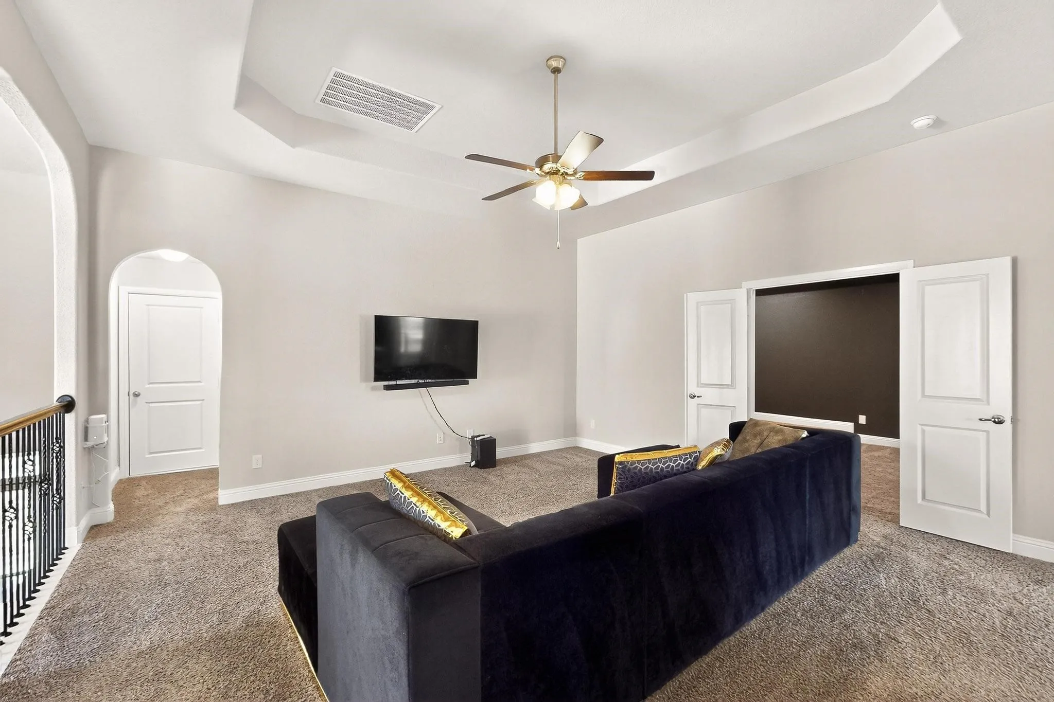 Living area with a tray ceiling, carpet, arched walkways, and a ceiling fan