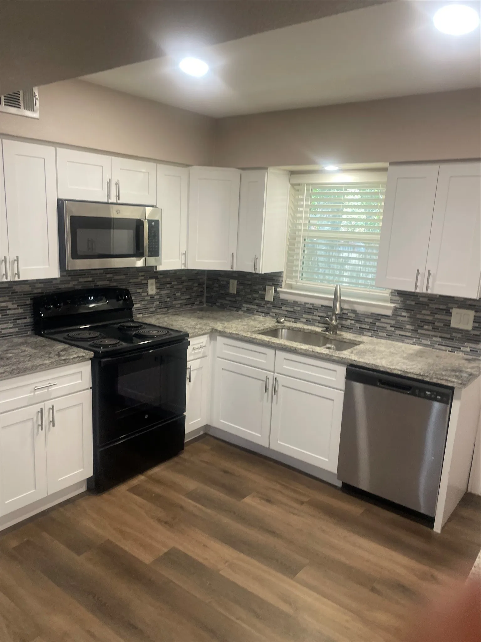 Kitchen with wood-finish flooring, white cabinetry, stainless steel appliances, mosaic tile backsplash, and recessed lighting