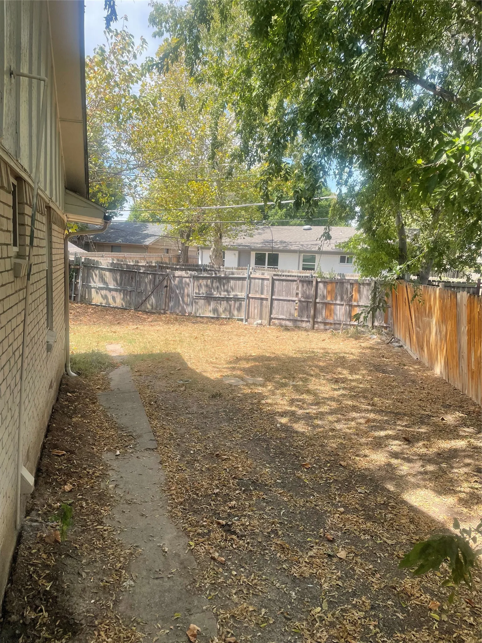 Fenced backyard with mature trees and a brick exterior