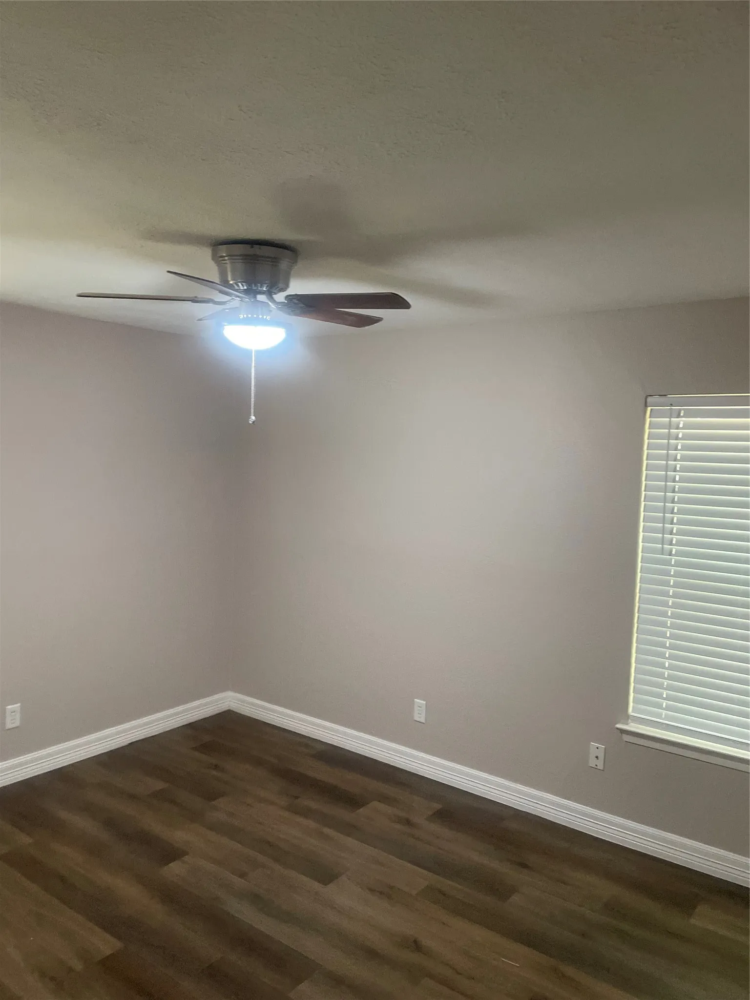 Neutral wall color, wood-finish flooring, ceiling fan with integrated lighting, window with horizontal blinds, and white trim