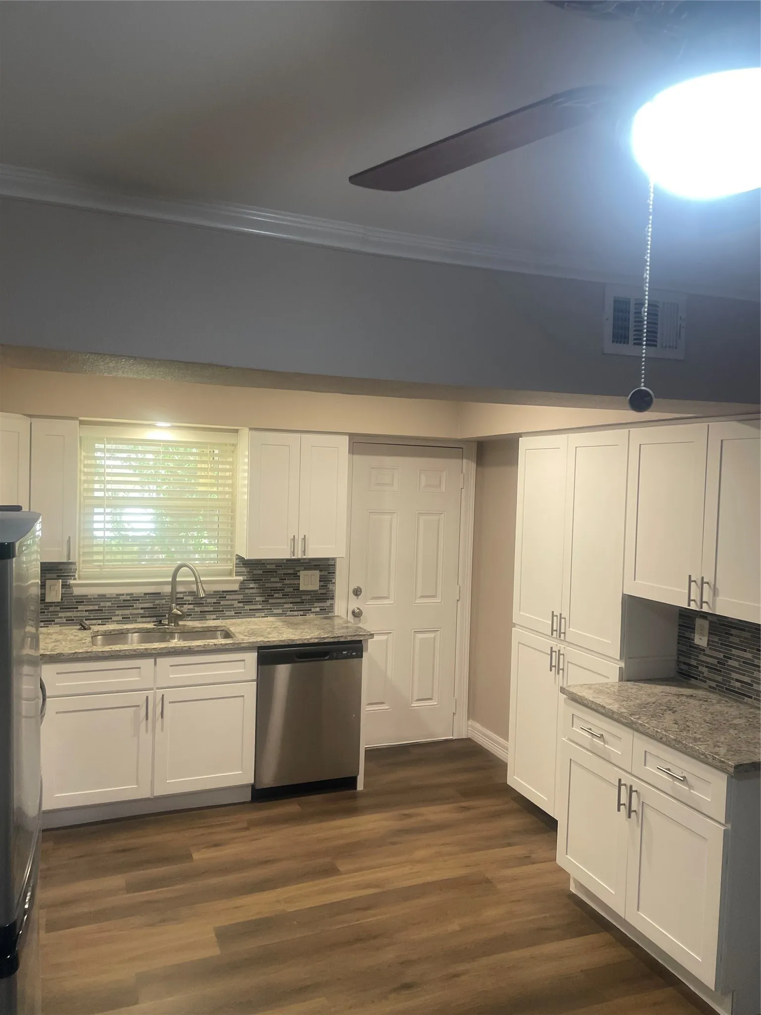 White cabinetry, stainless steel dishwasher, stone-finish countertops, tile backsplash, and wood-finish flooring