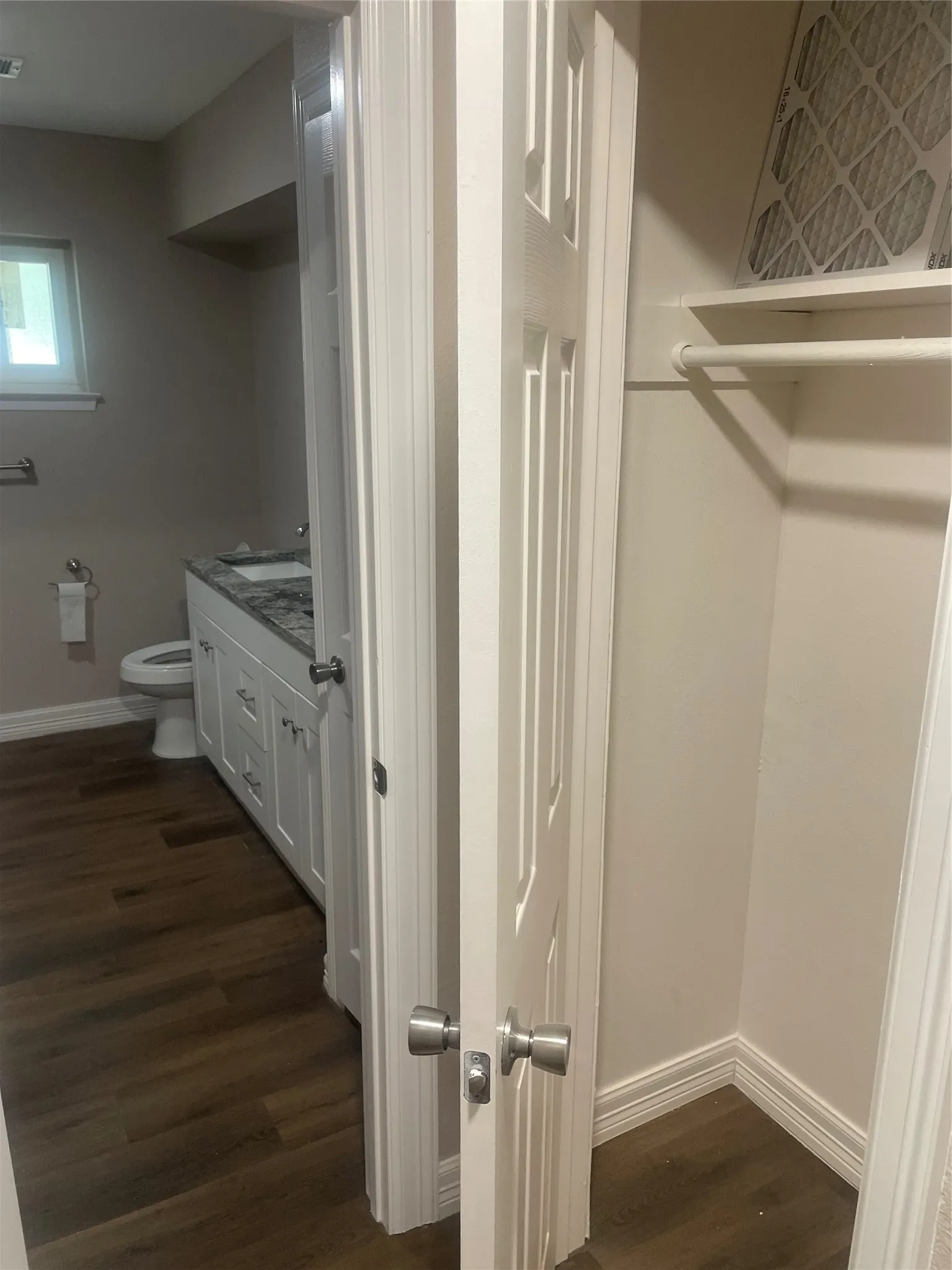 Bathroom featuring wood-finish flooring, a white vanity with granite-style countertop, and a built-in closet with shelving