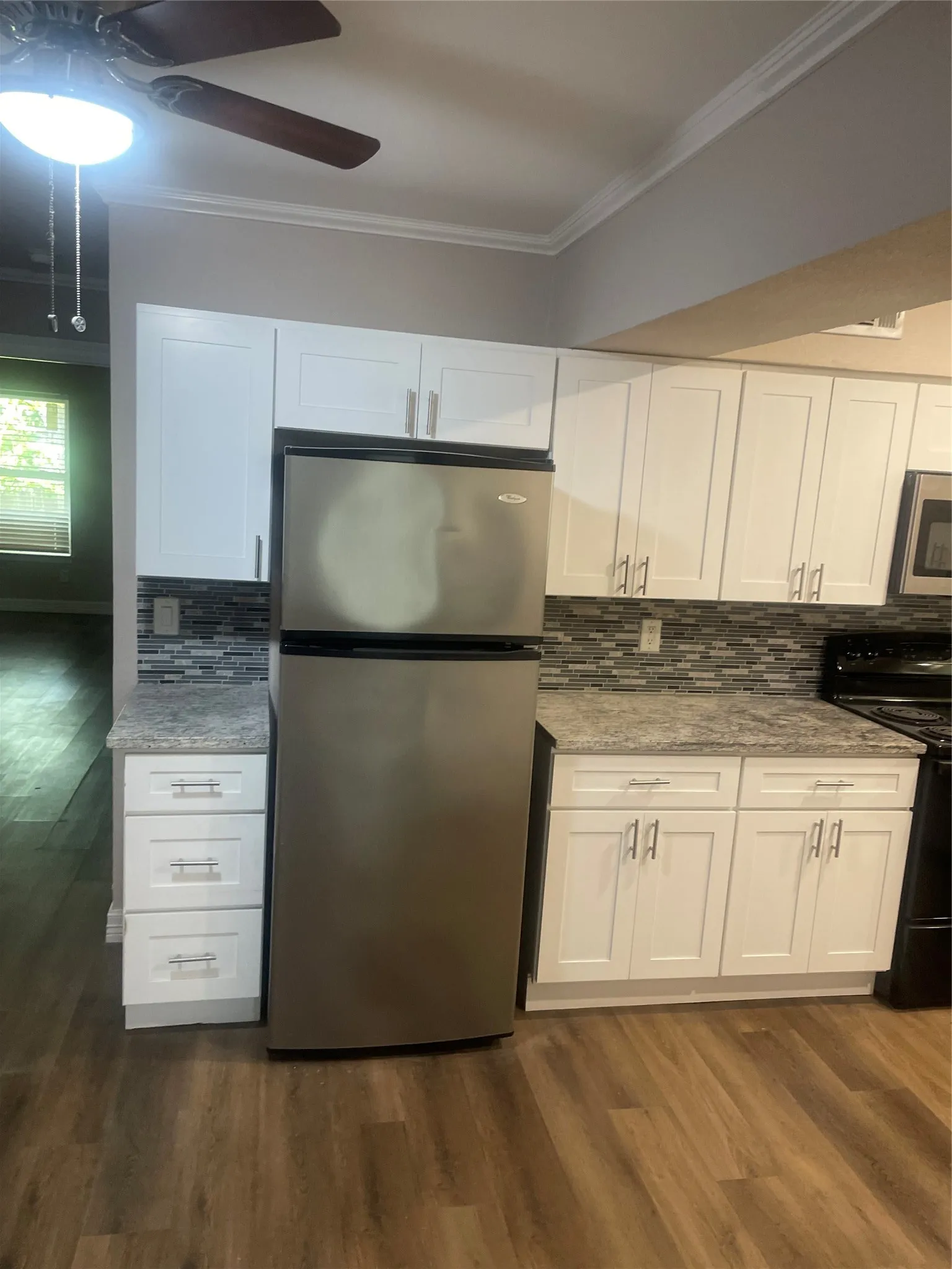 Kitchen featuring white cabinetry, gray patterned countertops, mosaic tile backsplash, stainless steel refrigerator, and wood-finish flooring