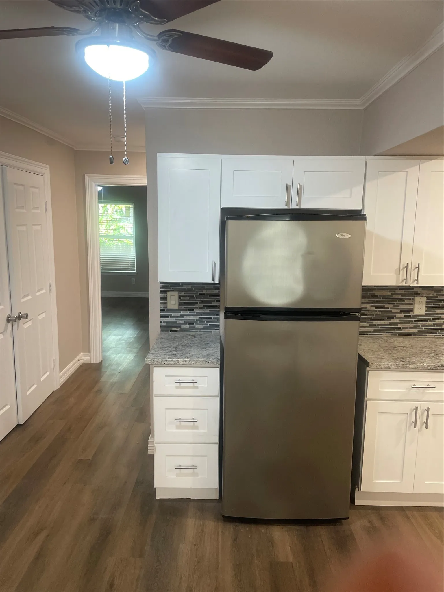 Kitchen featuring wood-finish flooring, white cabinetry, a stainless steel refrigerator, and mosaic tile backsplash