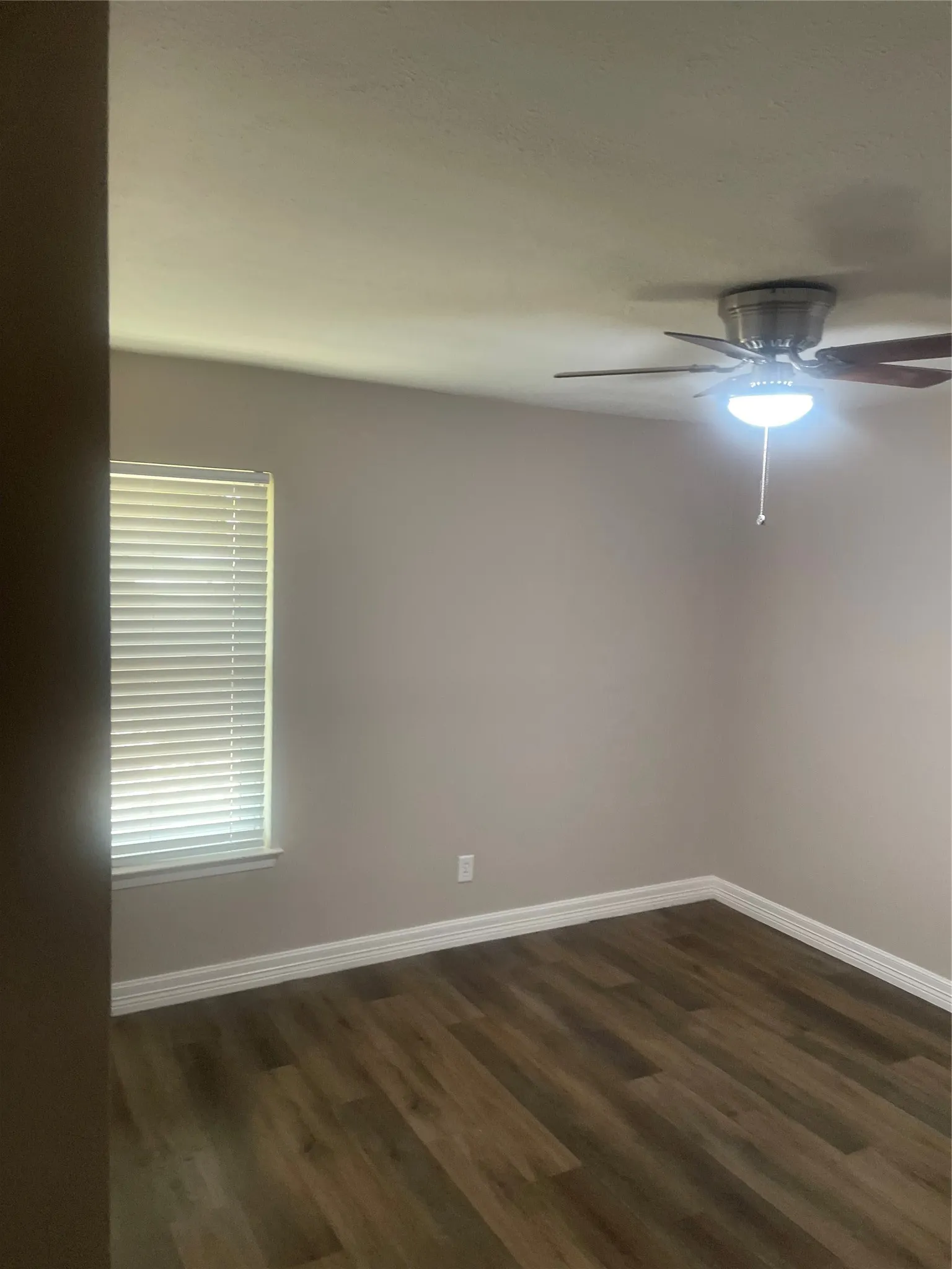 Wood-finish flooring, neutral wall tones, white trim, window with blinds, and a ceiling fan with integrated lighting