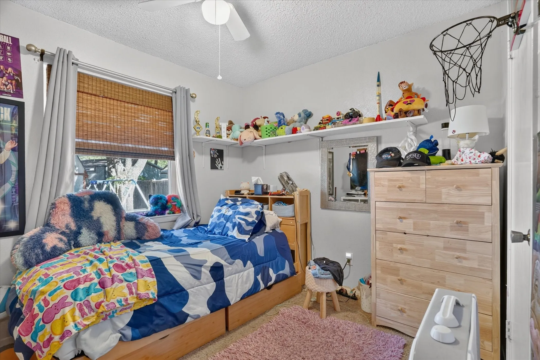 Window with woven wood blinds, ceiling fan, wall-mounted shelving, and wood-finish dresser