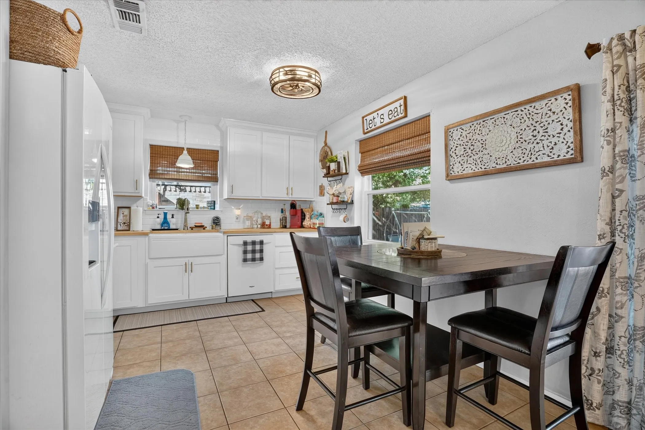 White cabinetry with gold-finish hardware, farmhouse sink, wood-finish countertops, ceramic tile flooring, and a flush-mount ceiling light fixture