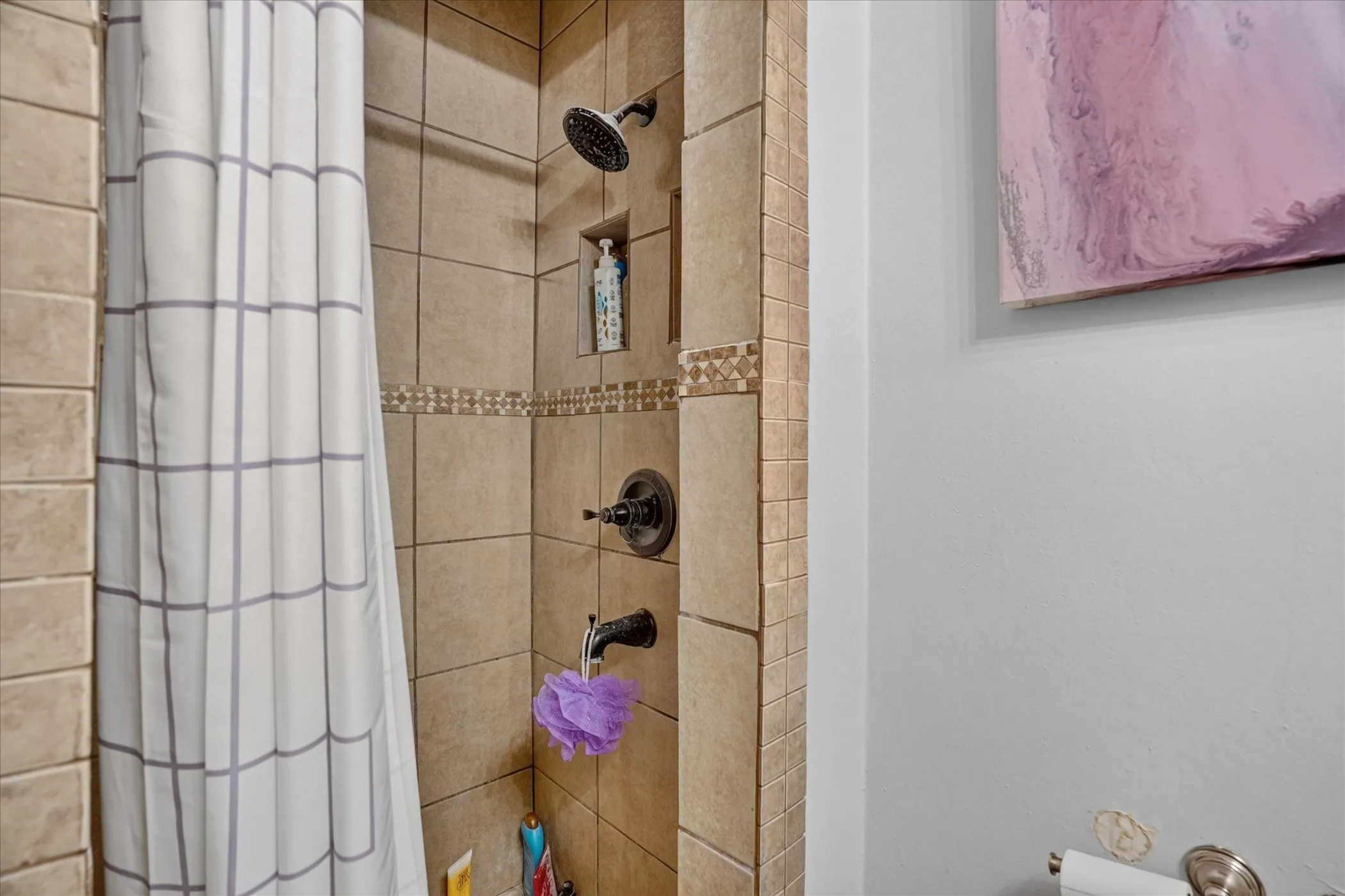 Tile shower with a built-in niche, decorative accent tile band, and dark bronze fixtures