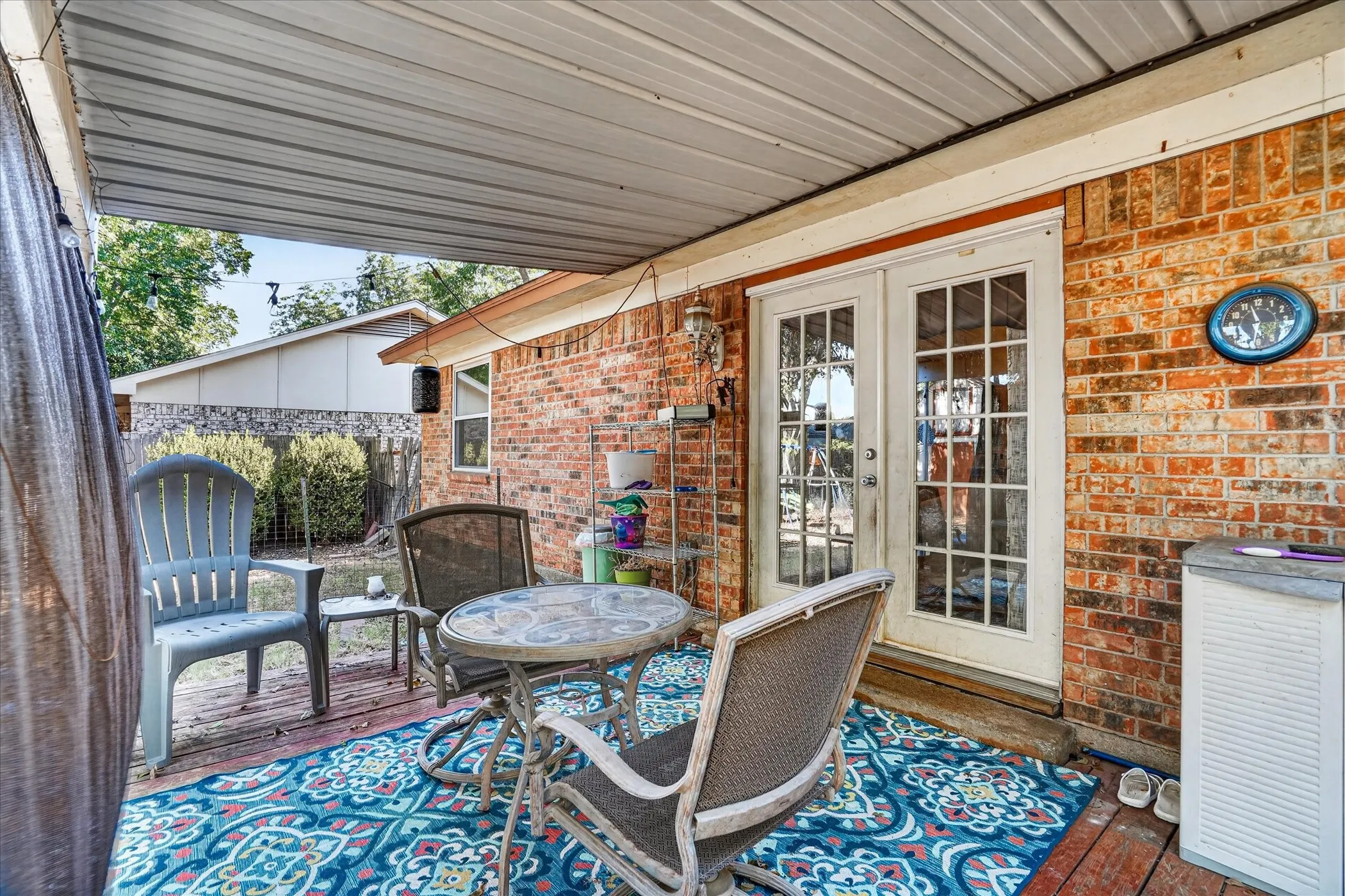 Covered patio with a corrugated metal ceiling, brick exterior, and white French doors