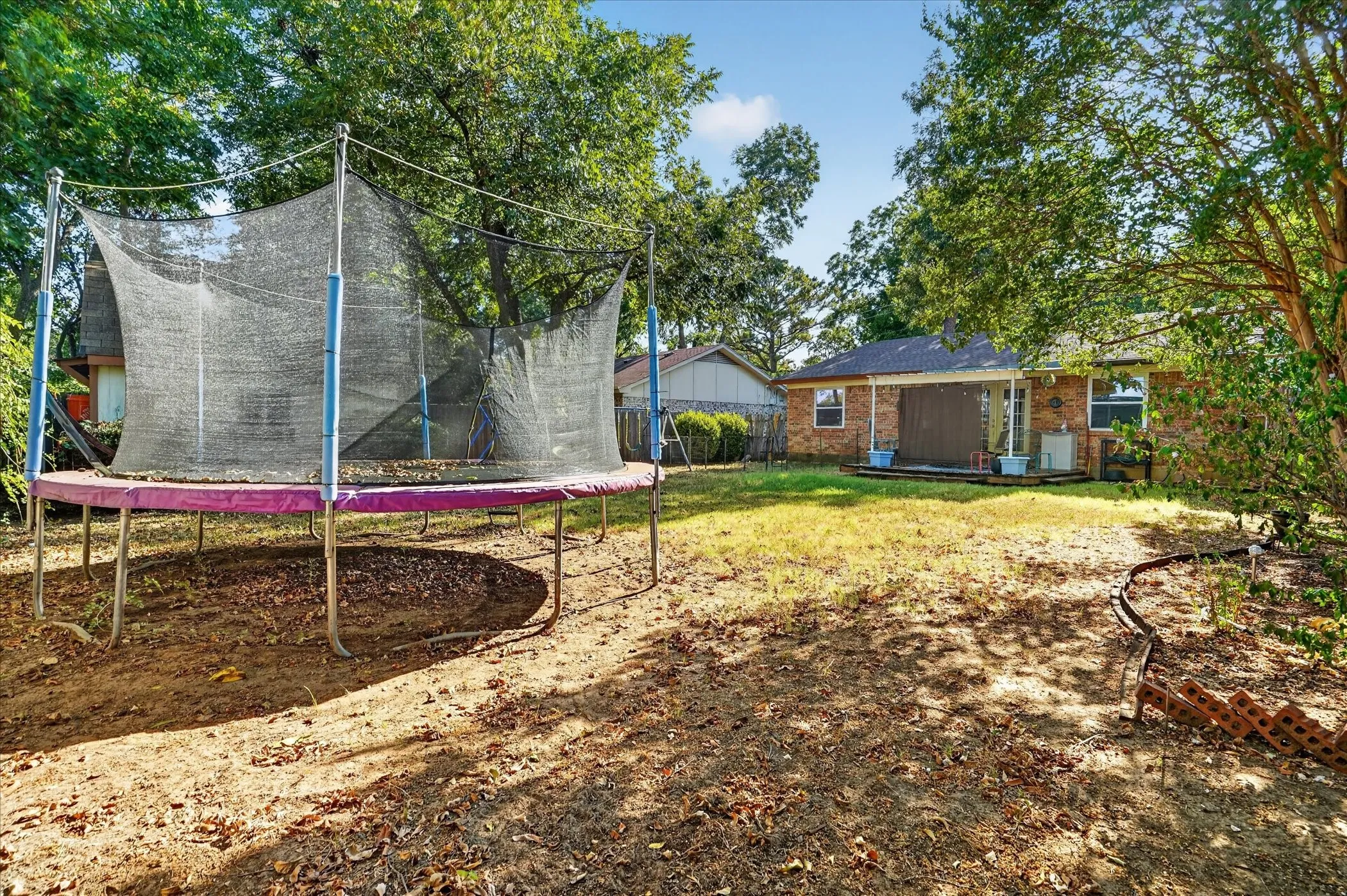 Expansive backyard featuring mature trees, a brick-faced exterior, a covered patio, and an outdoor HVAC unit