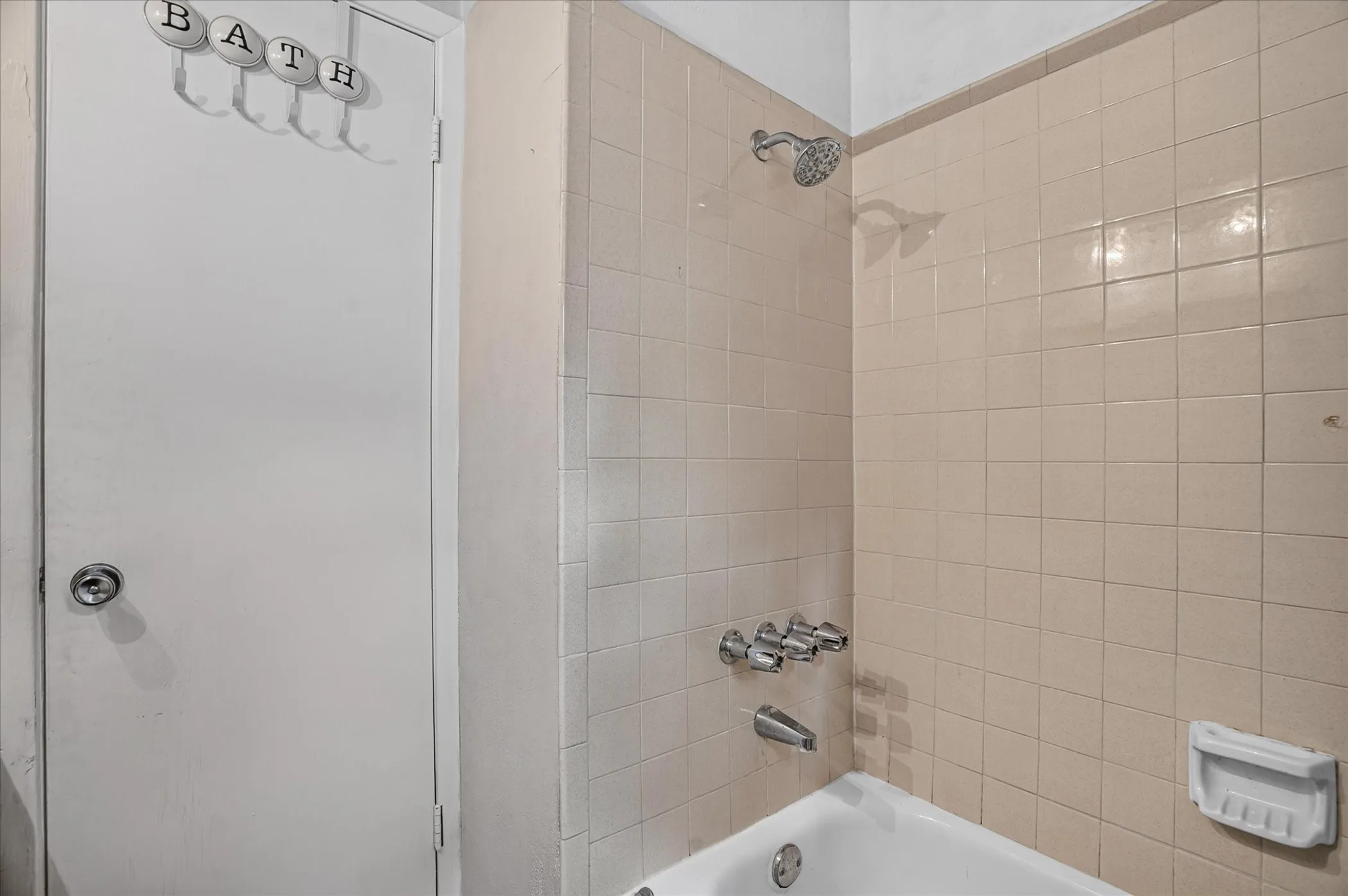 Bathtub with tiled surround, showerhead, and a three-handle fixture set