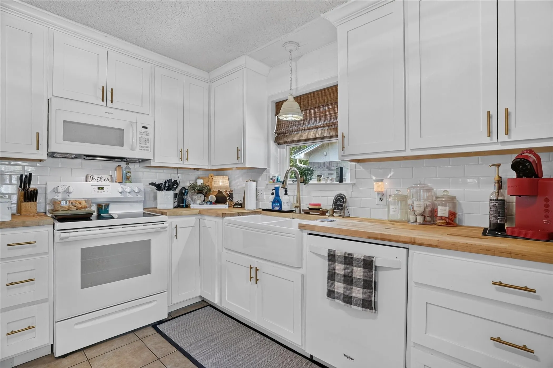 White shaker cabinetry, wood-finish countertops, white subway tile backsplash, white farmhouse sink, and stainless steel appliances