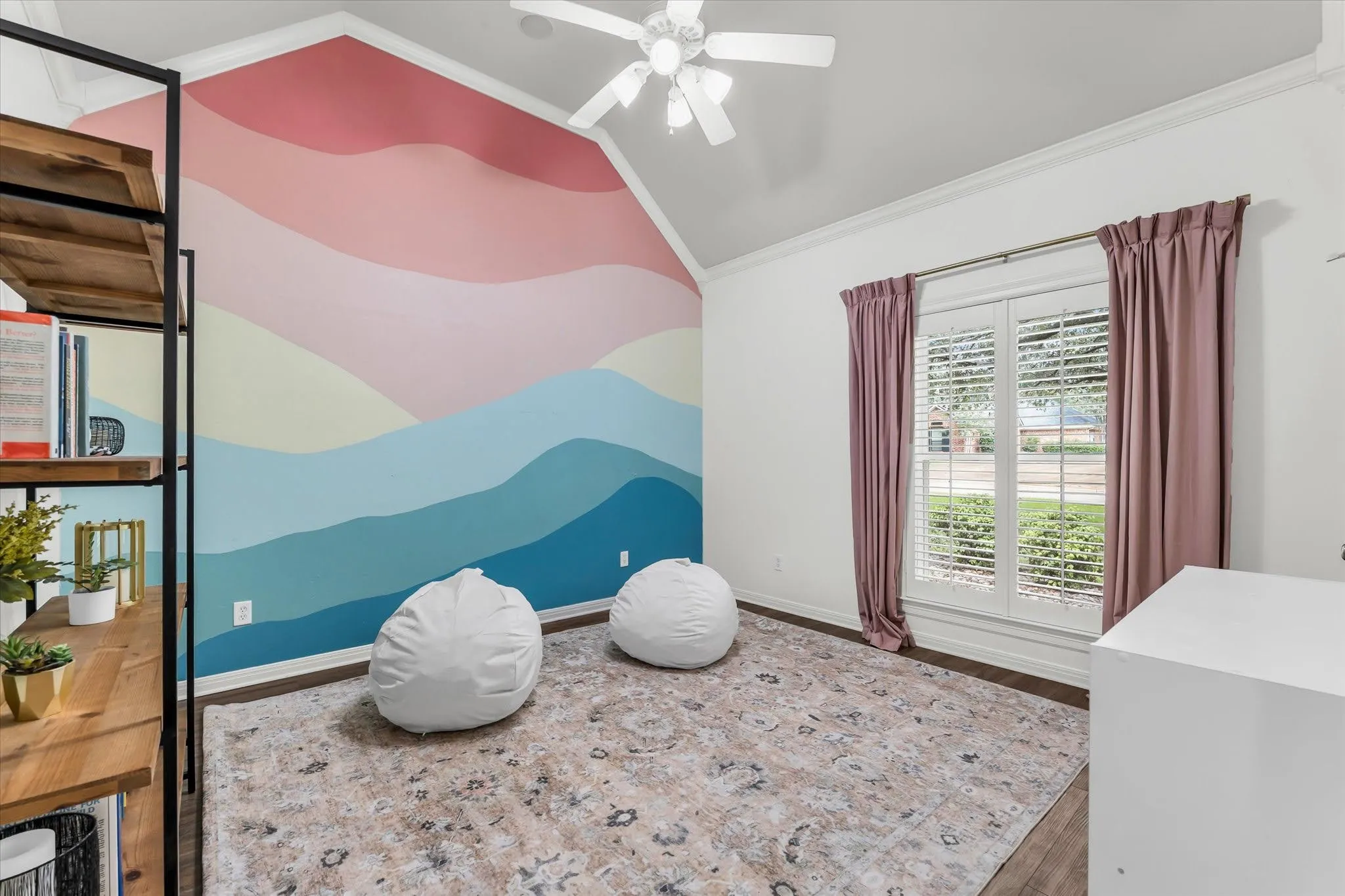 Vaulted ceiling with a ceiling fan, window with plantation shutters, wood-finish flooring, and a decorative accent wall
