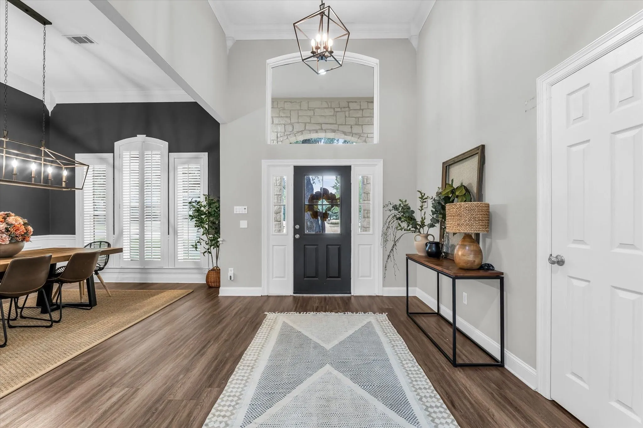 Vaulted entry with wood-finish flooring, a dark paneled front door, and a geometric pendant light fixture