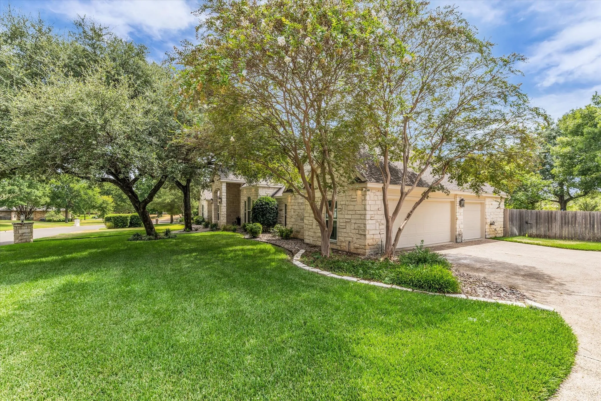 Stone exterior with a three-car garage, mature trees, and a concrete driveway