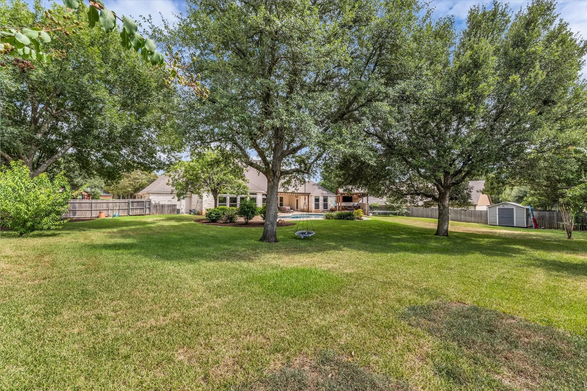 Expansive backyard featuring a manicured lawn, mature trees, and privacy fencing