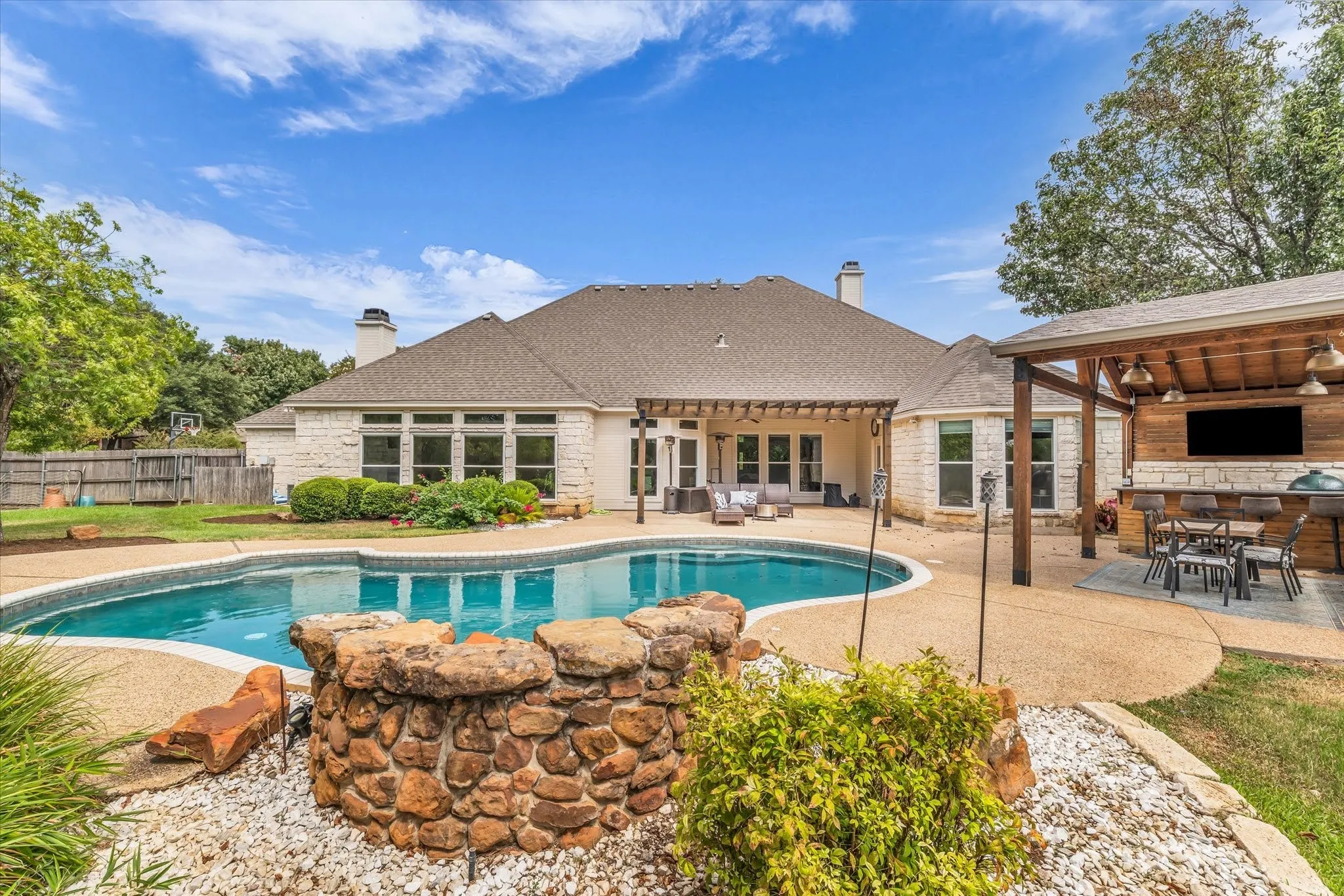 Spacious backyard featuring a built-in swimming pool, extended patio with a pergola, and an outdoor kitchen