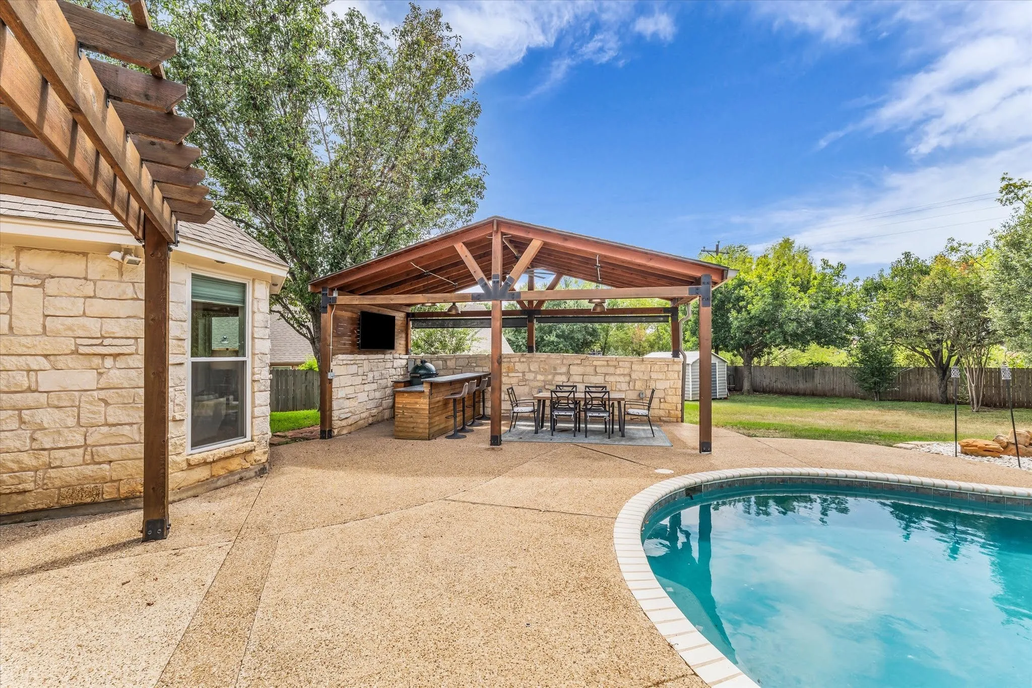 Expansive outdoor living area featuring a covered patio, built-in outdoor kitchen, and a swimming pool with a stone coping
