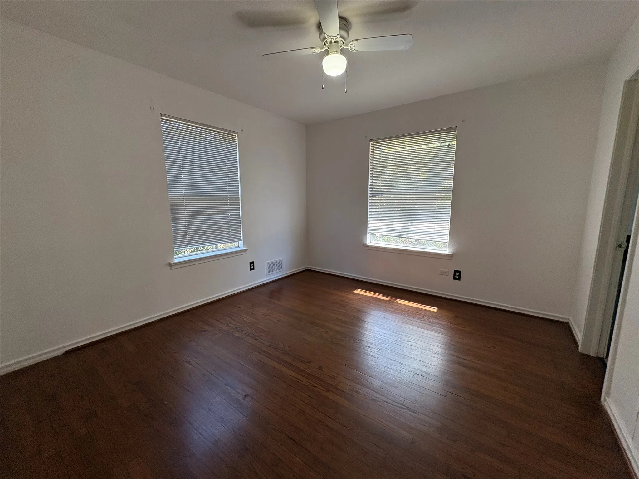 Hardwood flooring, two windows with blinds, ceiling fan with integrated lighting, and white wall finishes