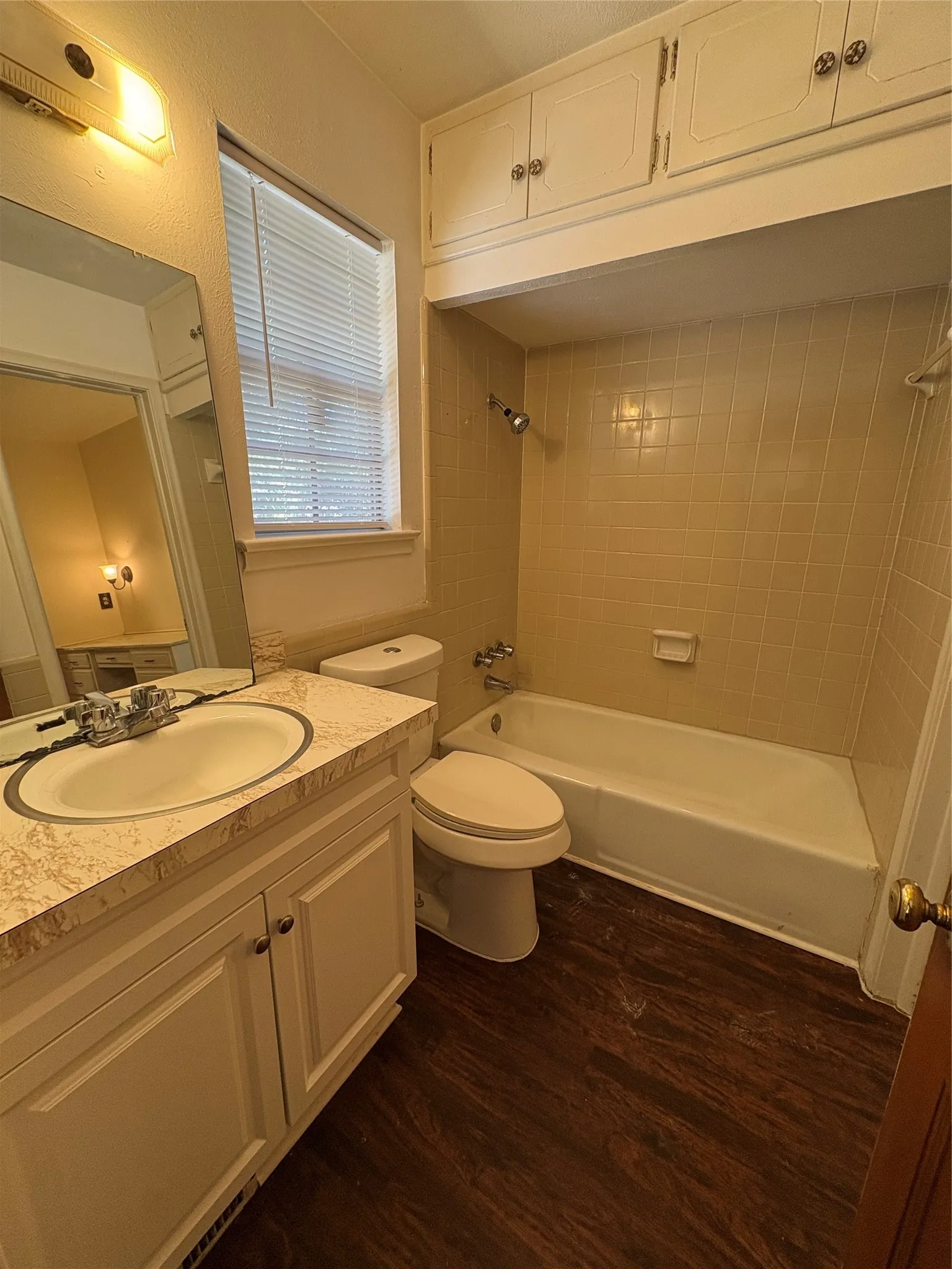 Bathroom featuring a single vanity with an integrated sink, built-in storage above the tub, a bathtub with shower, and wood-finish flooring