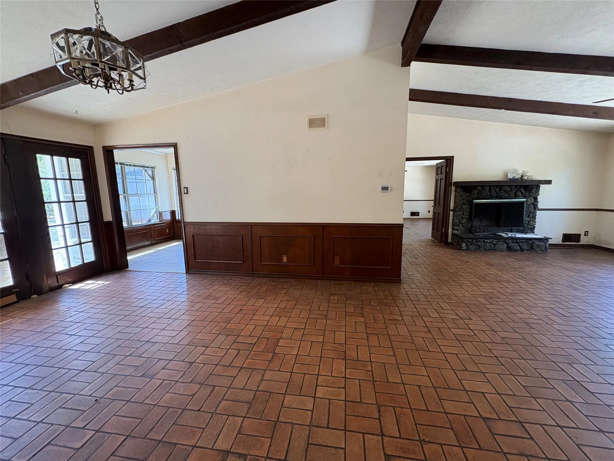 Vaulted ceilings with exposed wood beams, brick-patterned flooring, wood wainscoting, and a stone fireplace
