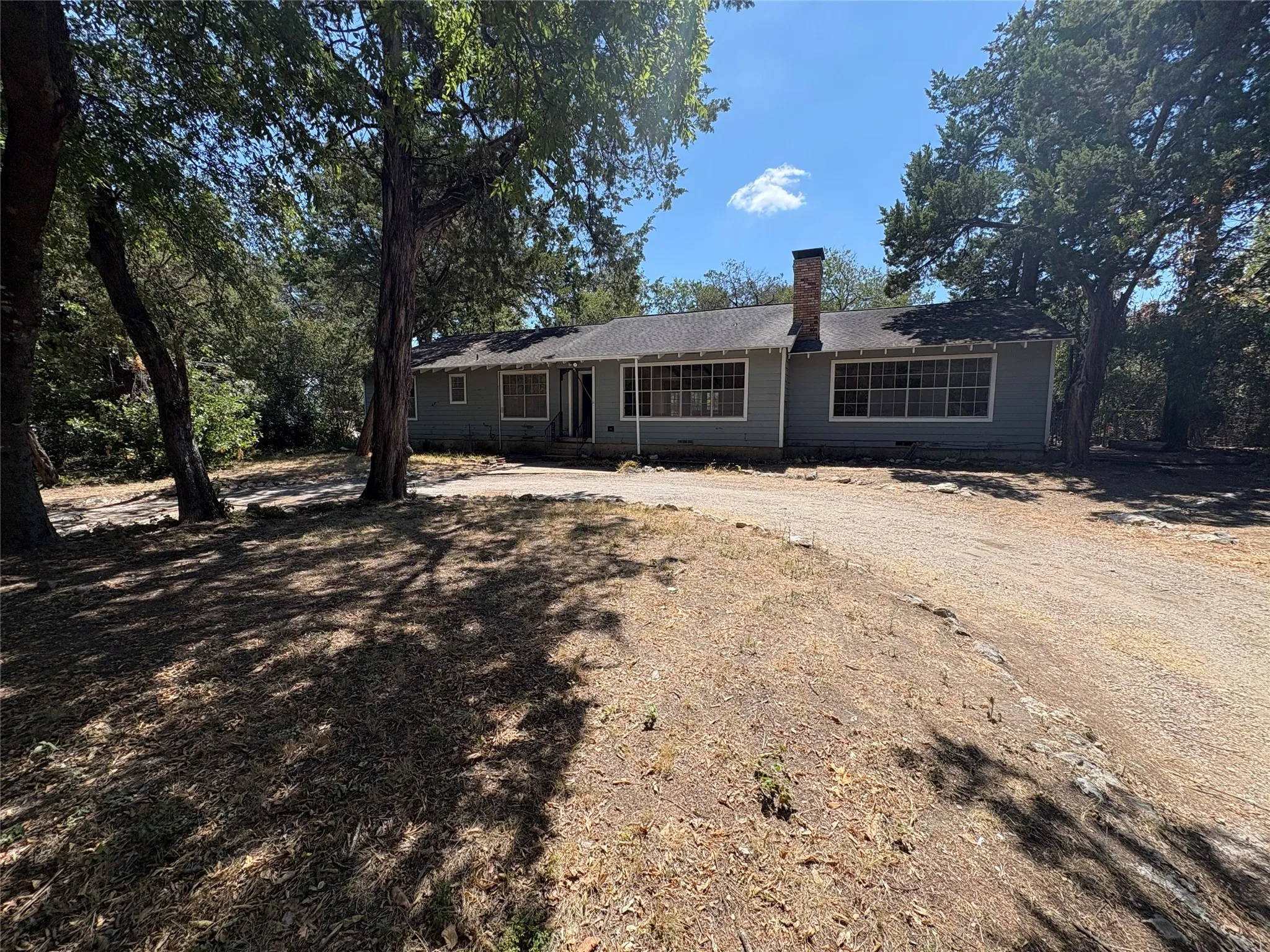 Single-story residence with a gray exterior, prominent brick chimney, and a gravel driveway