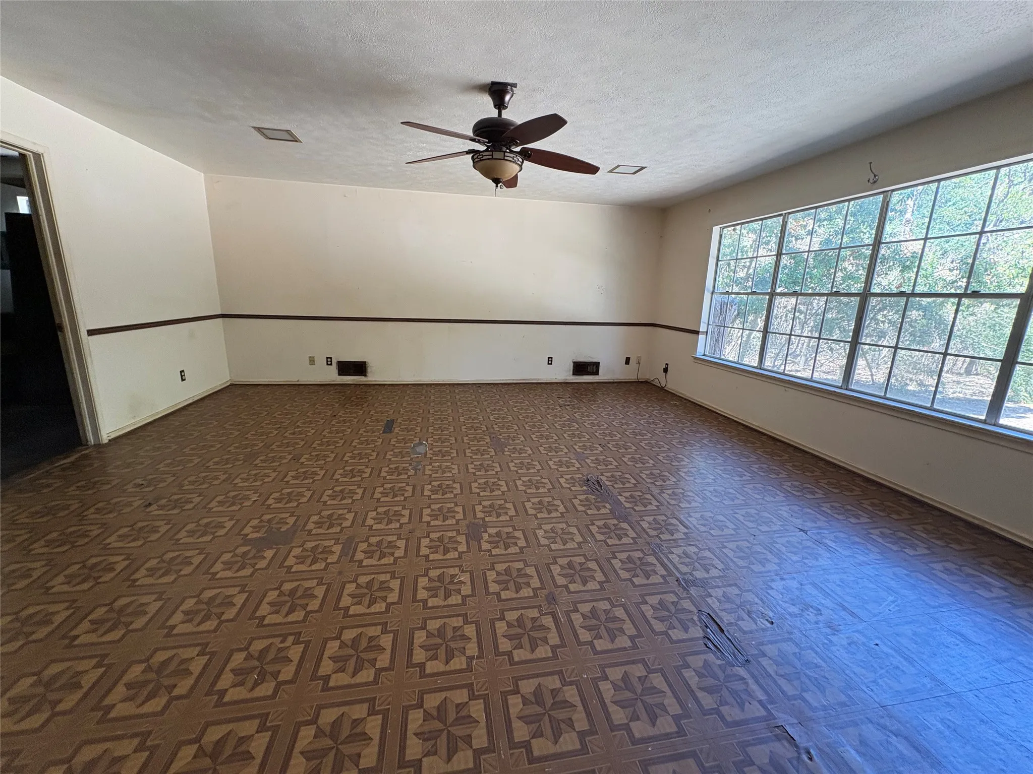 Spacious room featuring patterned flooring, extensive window, and a ceiling fan with integrated lighting