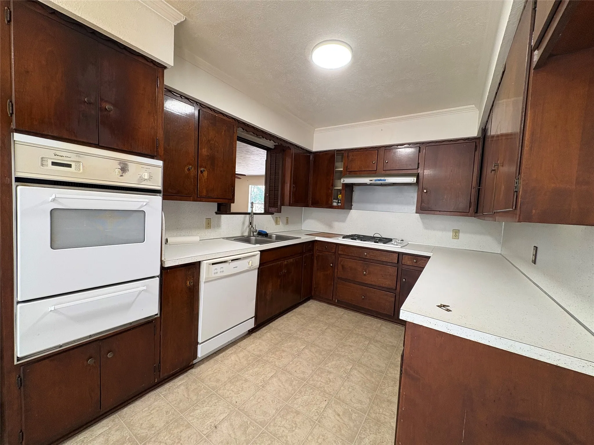Kitchen with wood cabinetry, white countertops, a built-in double oven, a dishwasher, and a range cooktop
