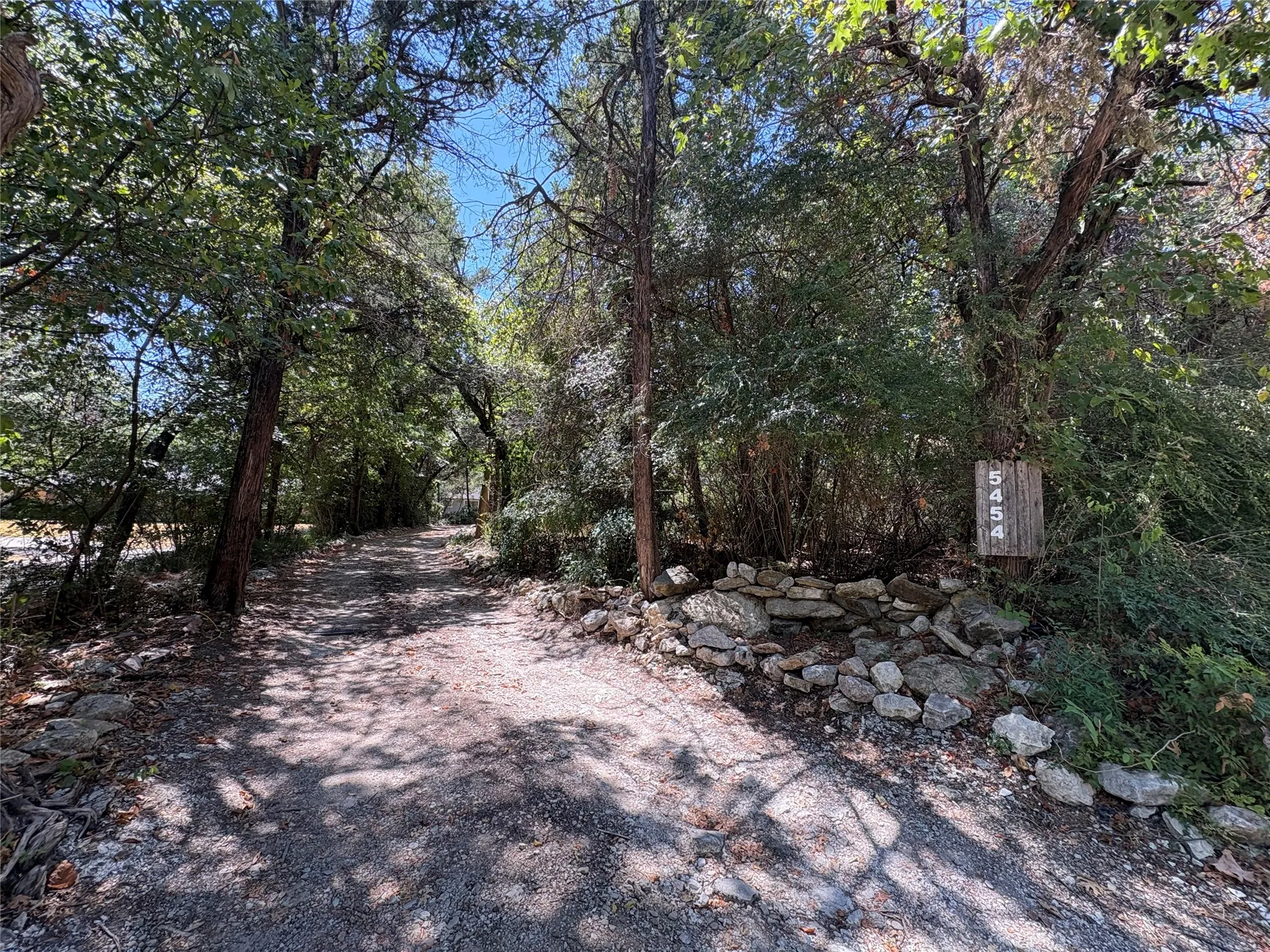 Gravel drive with surrounding mature trees and natural stone border