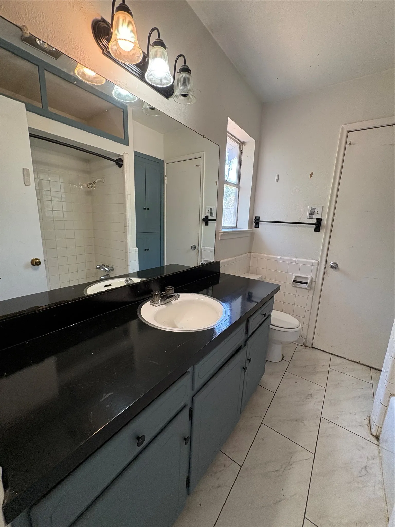 Dual basin vanity with a dark countertop and integrated sinks, white subway tile shower surround, and a built-in storage cabinet