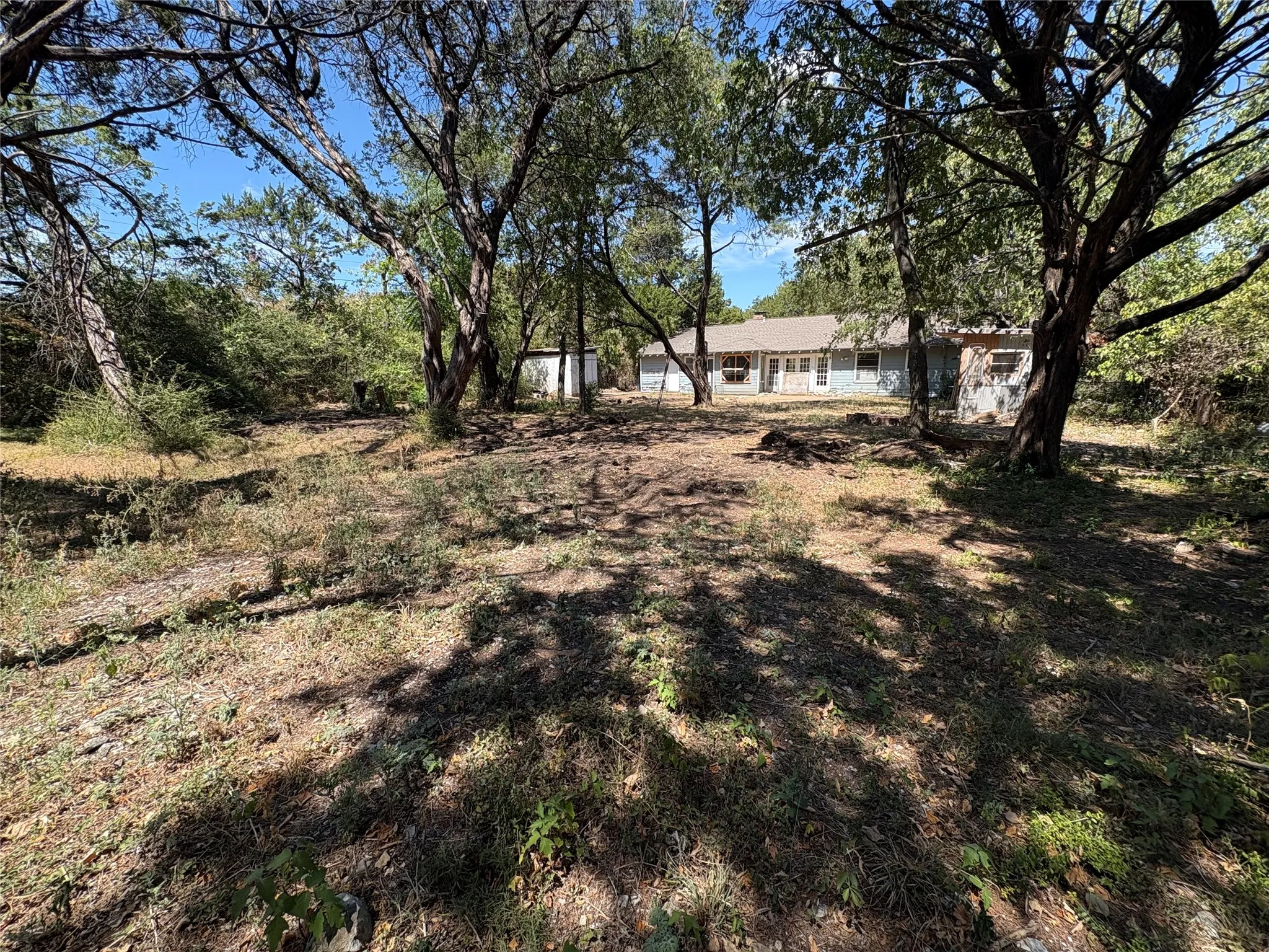 Expansive lot featuring mature trees and established ground cover, with a single-story residence and detached structure in the background
