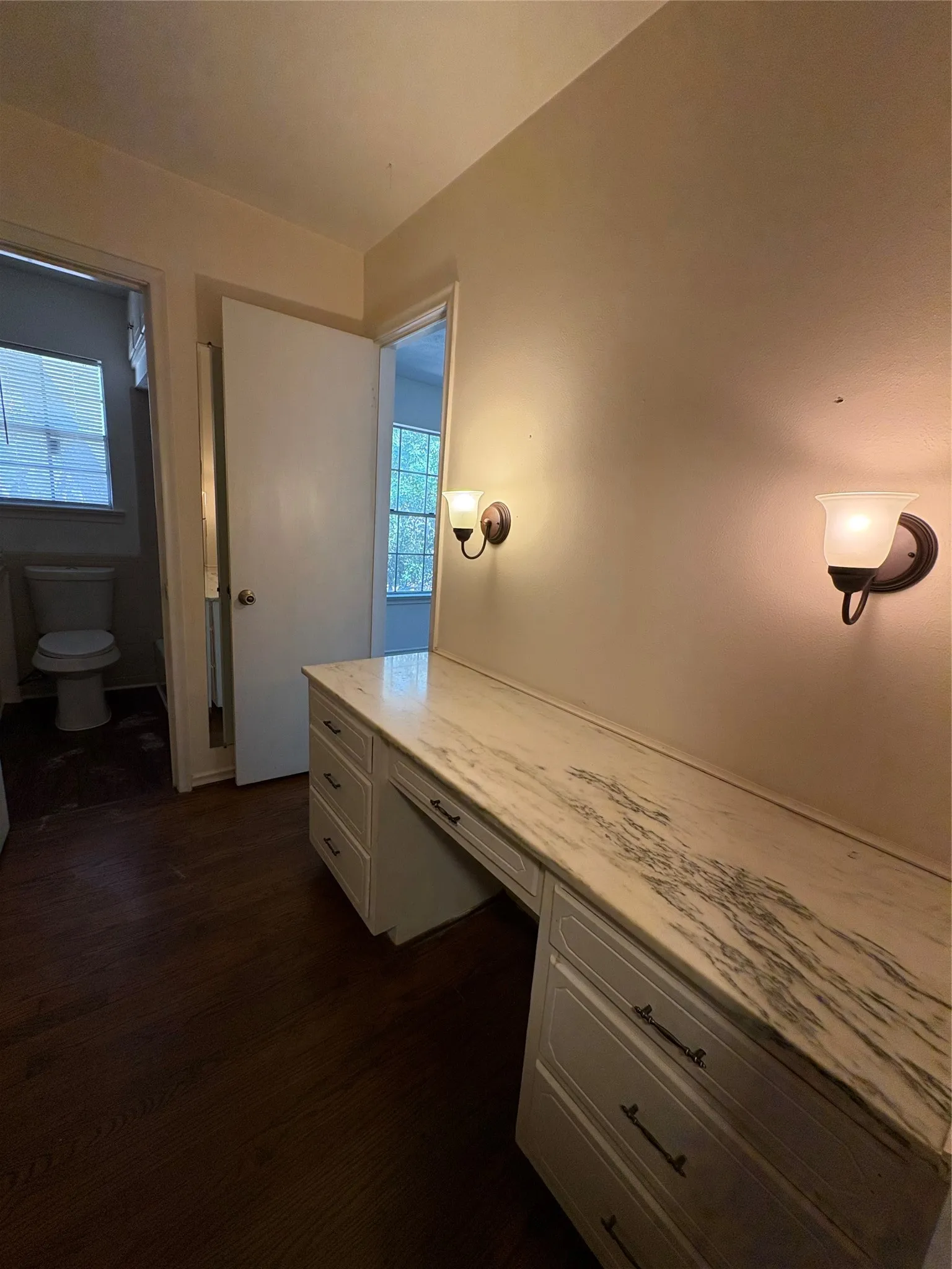 Built-in vanity with a stone countertop, sconce lighting, and wood-finish flooring