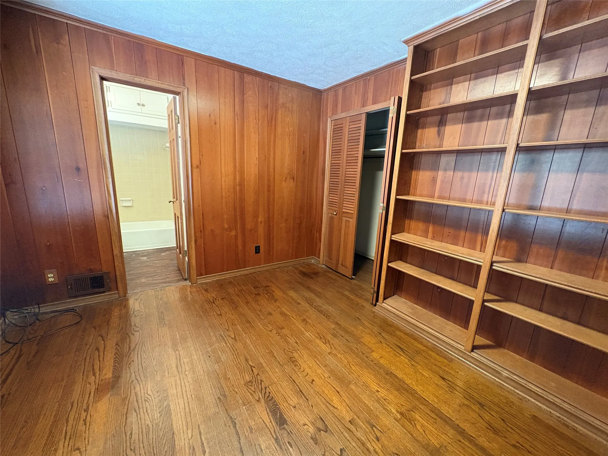 Wood paneling throughout, hardwood flooring, built-in shelving, and bifold closet doors
